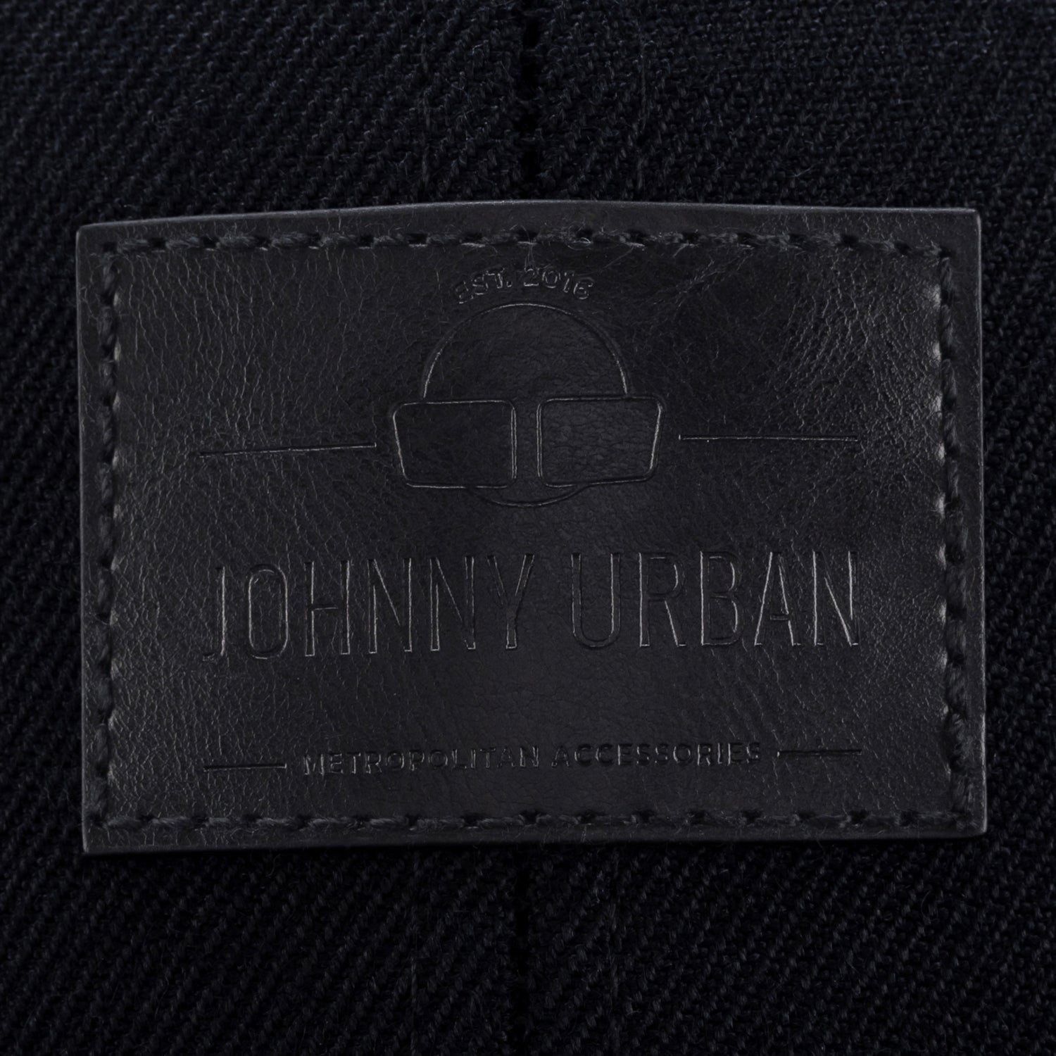 Schwarzes Lederetikett mit eingeprägtem Logo und Text 'Johnny Urban', auf dunklem Stoff mit sichtbarer Naht