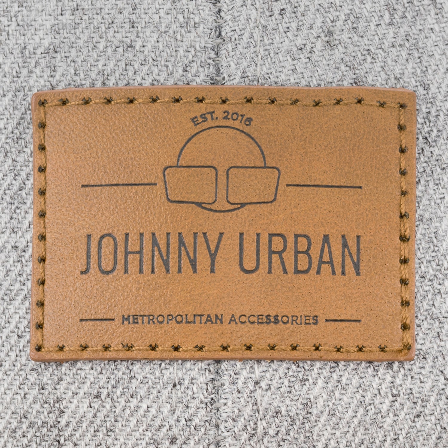 Nahtloses braunes Lederetikett mit Johnny Urban-Logo und Schriftzug auf grauer Textilstruktur