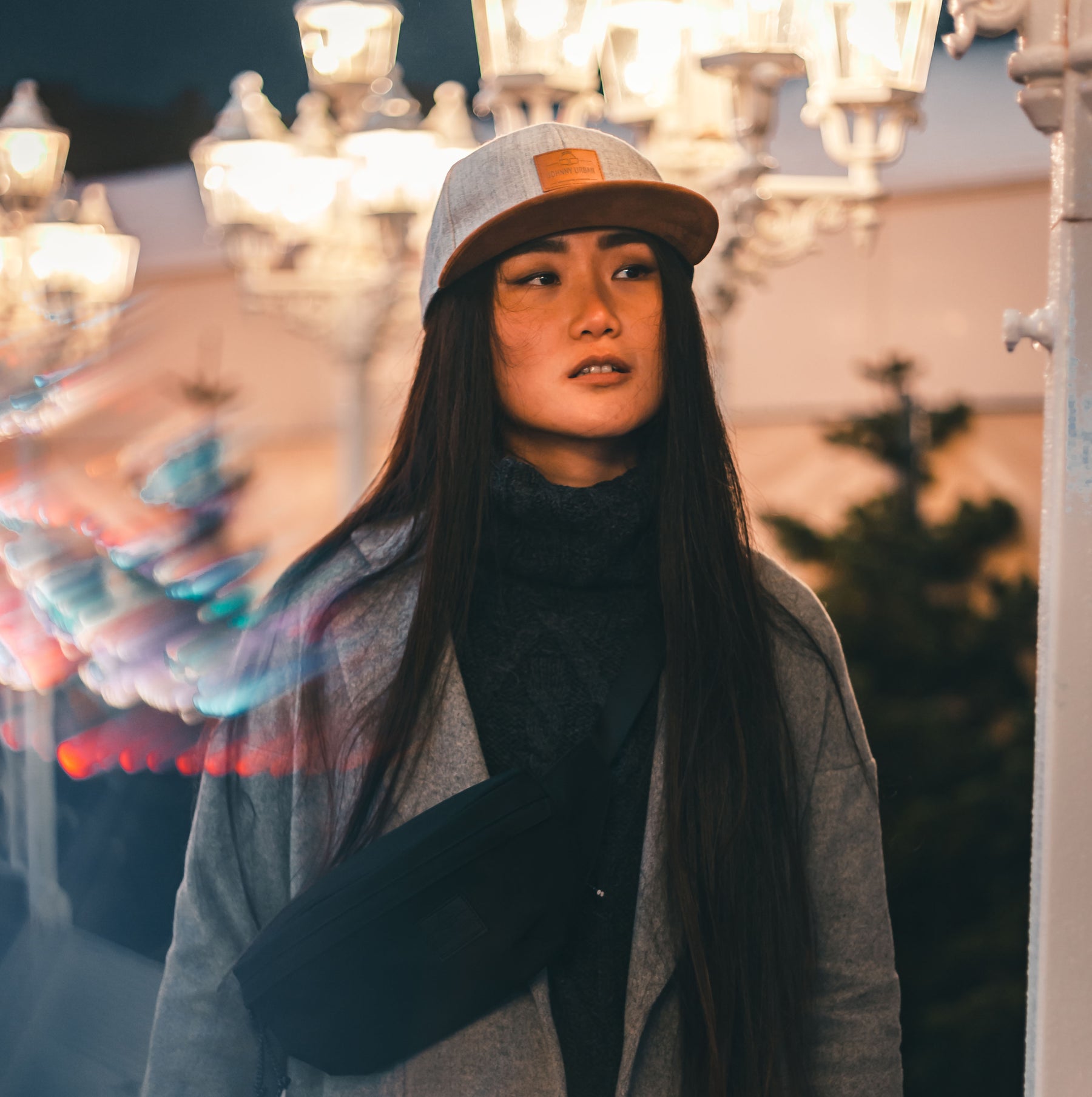 Frau mit langem dunklem Haar trägt graue Cap 'Dean' und schwarzen Schal bei Nacht im urbanen Umfeld mit Straßenlaternen