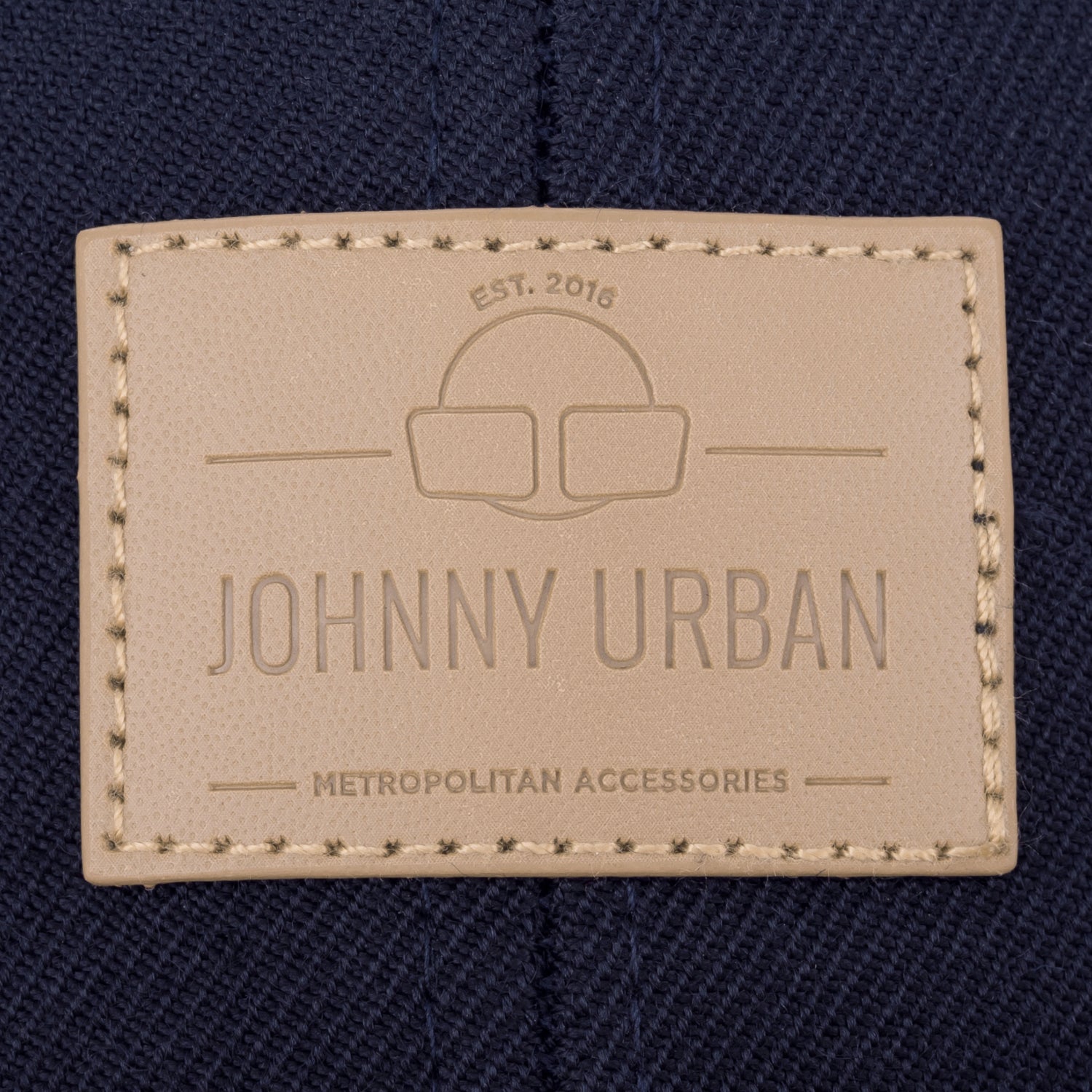 Beige geprägtes Lederetikett mit 'Johnny Urban', 'EST. 2016' und 'Metropolitan Accessories' auf dunkelblauem Stoff