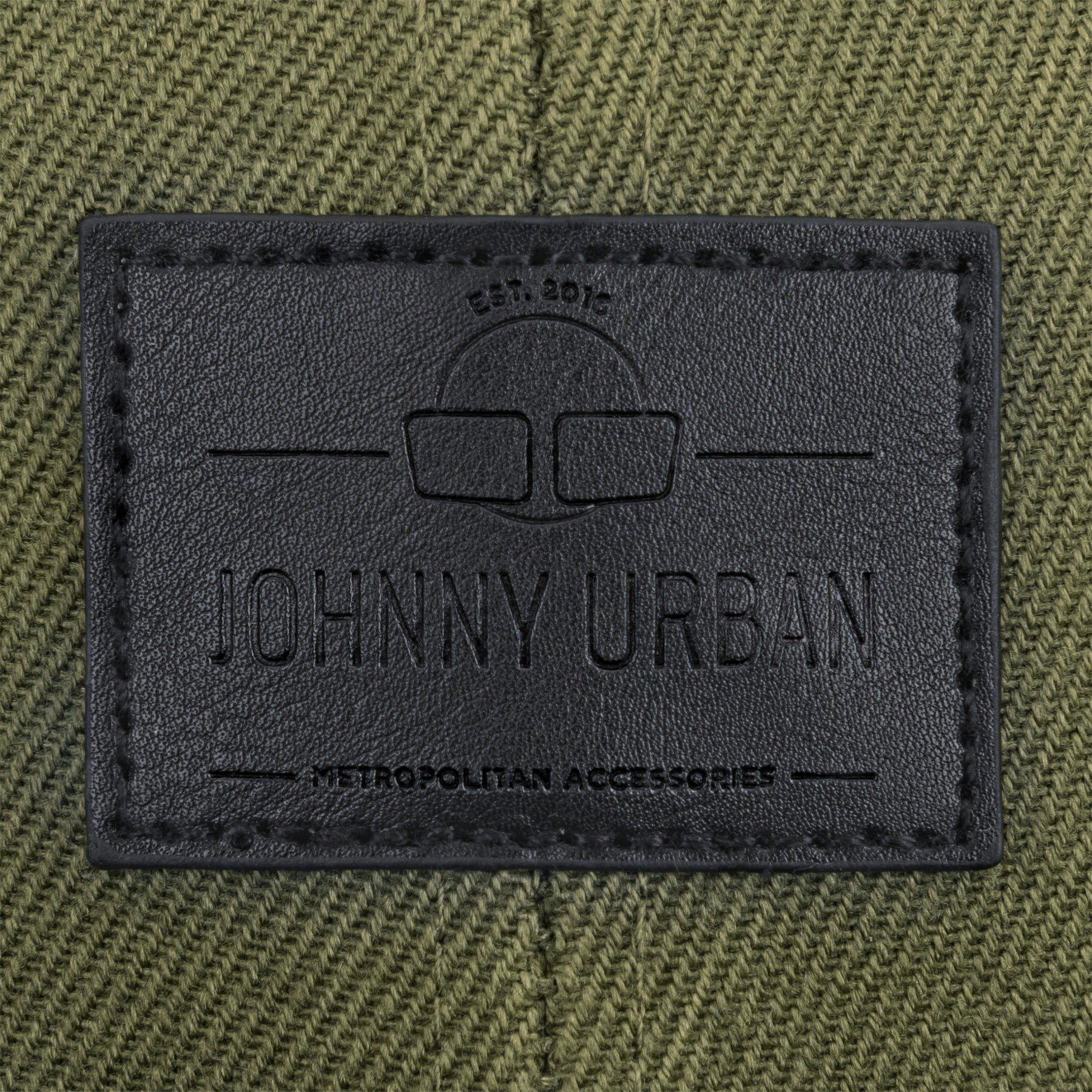 Schwarzes Lederlabel mit eingeprägtem Johnny Urban Logo und Text auf grünem Stoff