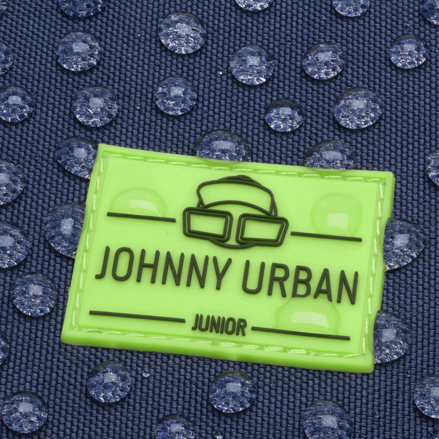 Nahe Aufnahme eines wasserabweisenden dunkelblauen Stoffes mit aufgenähtem neongrünem Johnny Urban Junior Logo-Patch
