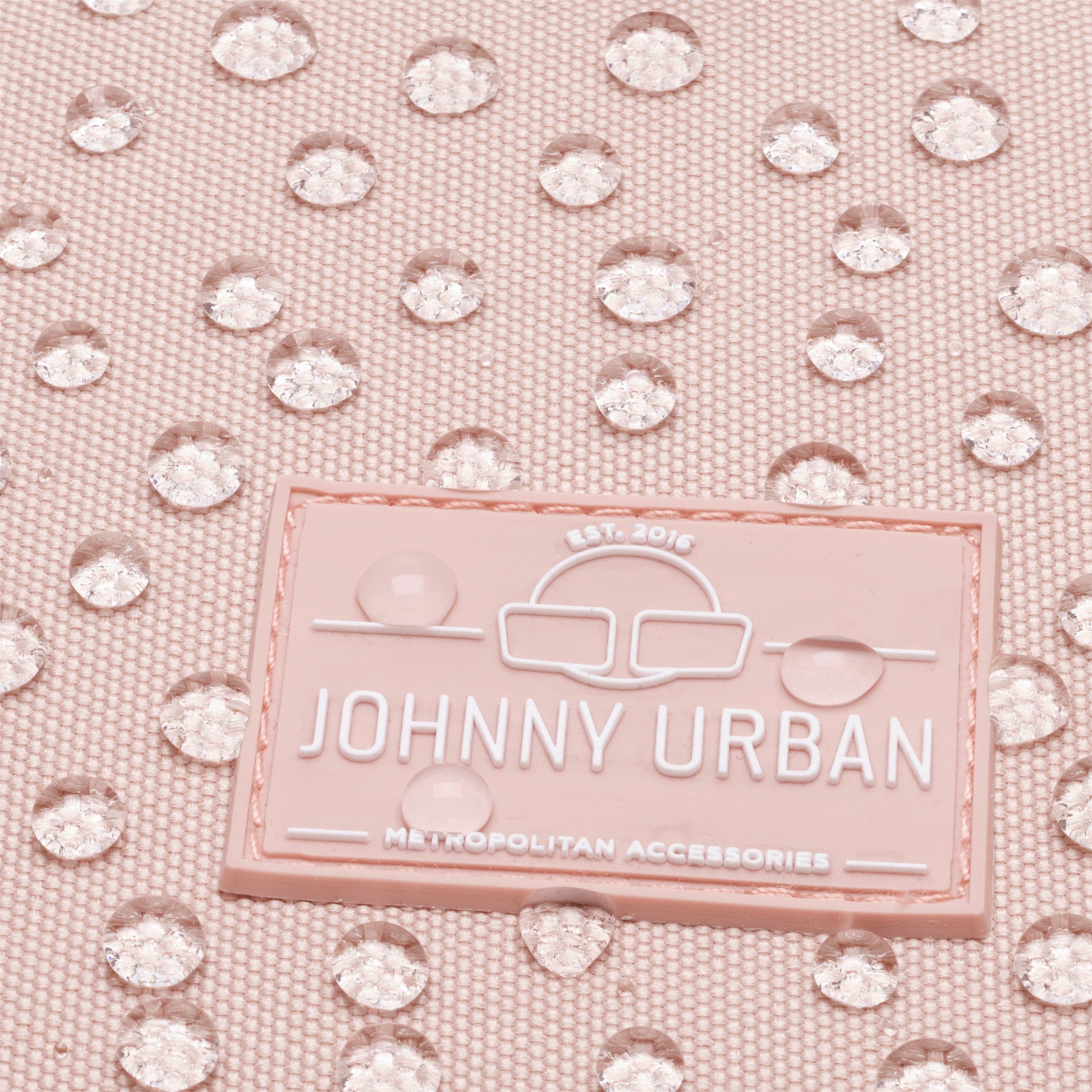 Nahaufnahme des JOHNNY URBAN Logos auf einem rosa wasserdichten Damenrucksack Romy mit Wassertropfen