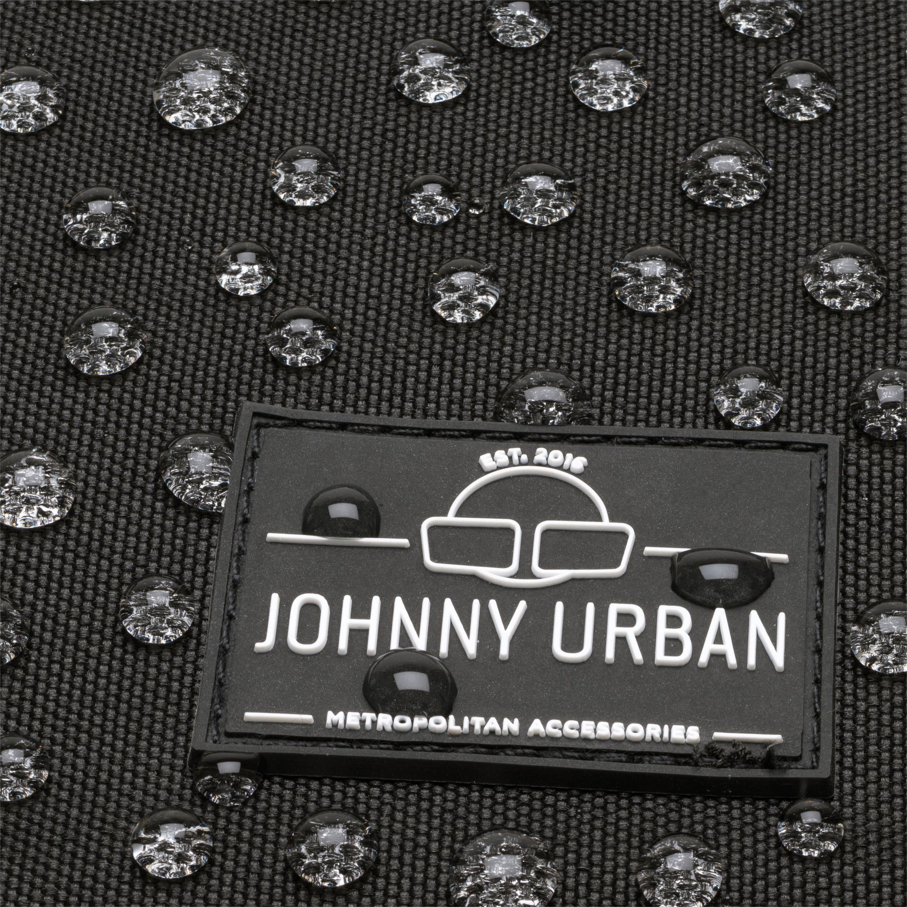 Nahaufnahme des Johnny Urban Logos auf wasserdichtem schwarzen Gewebe mit Wasserperlen