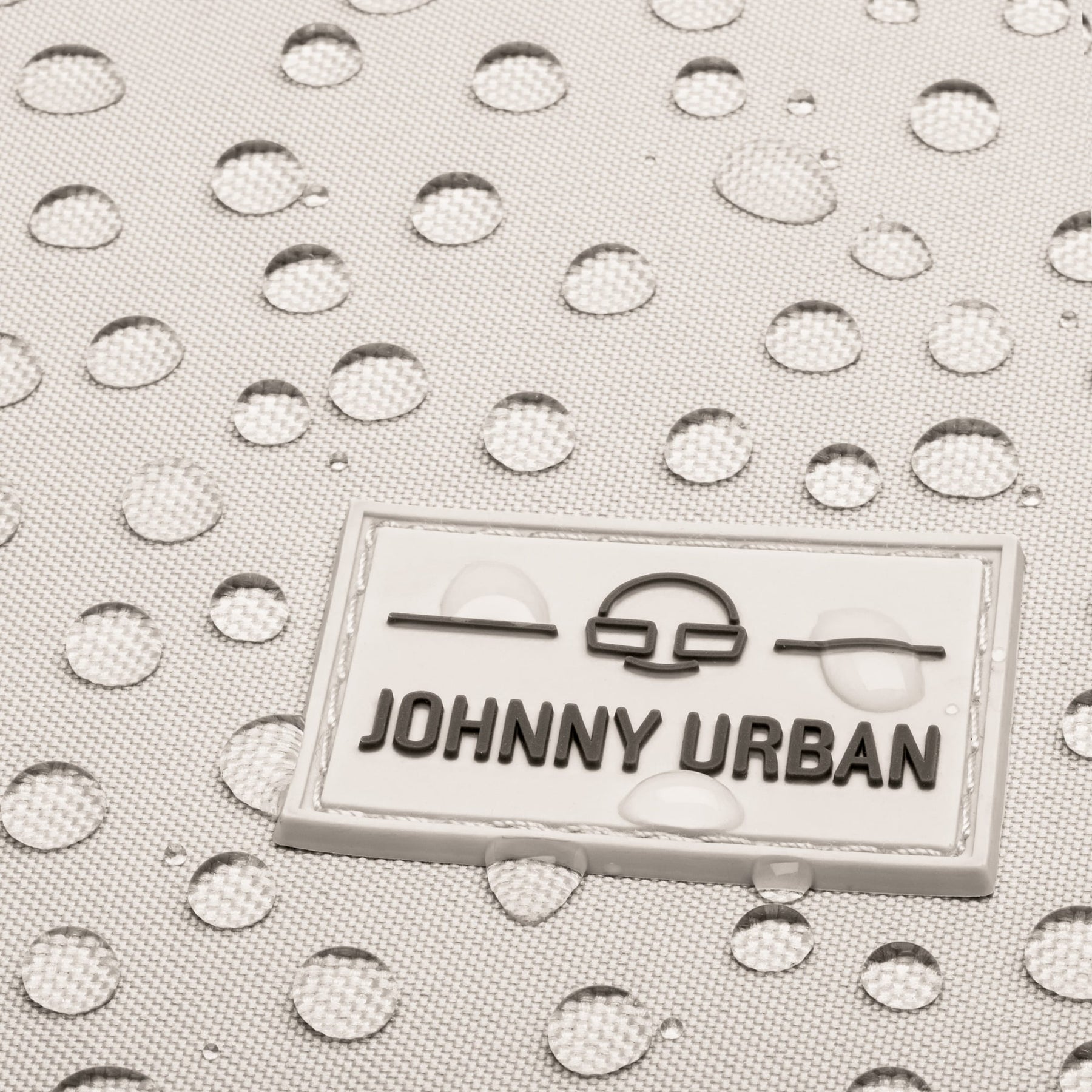 Nahaufnahme des wasserabweisenden Materials des sandgrauen Rucksacks 'Jona Small' mit Johnny Urban Logo