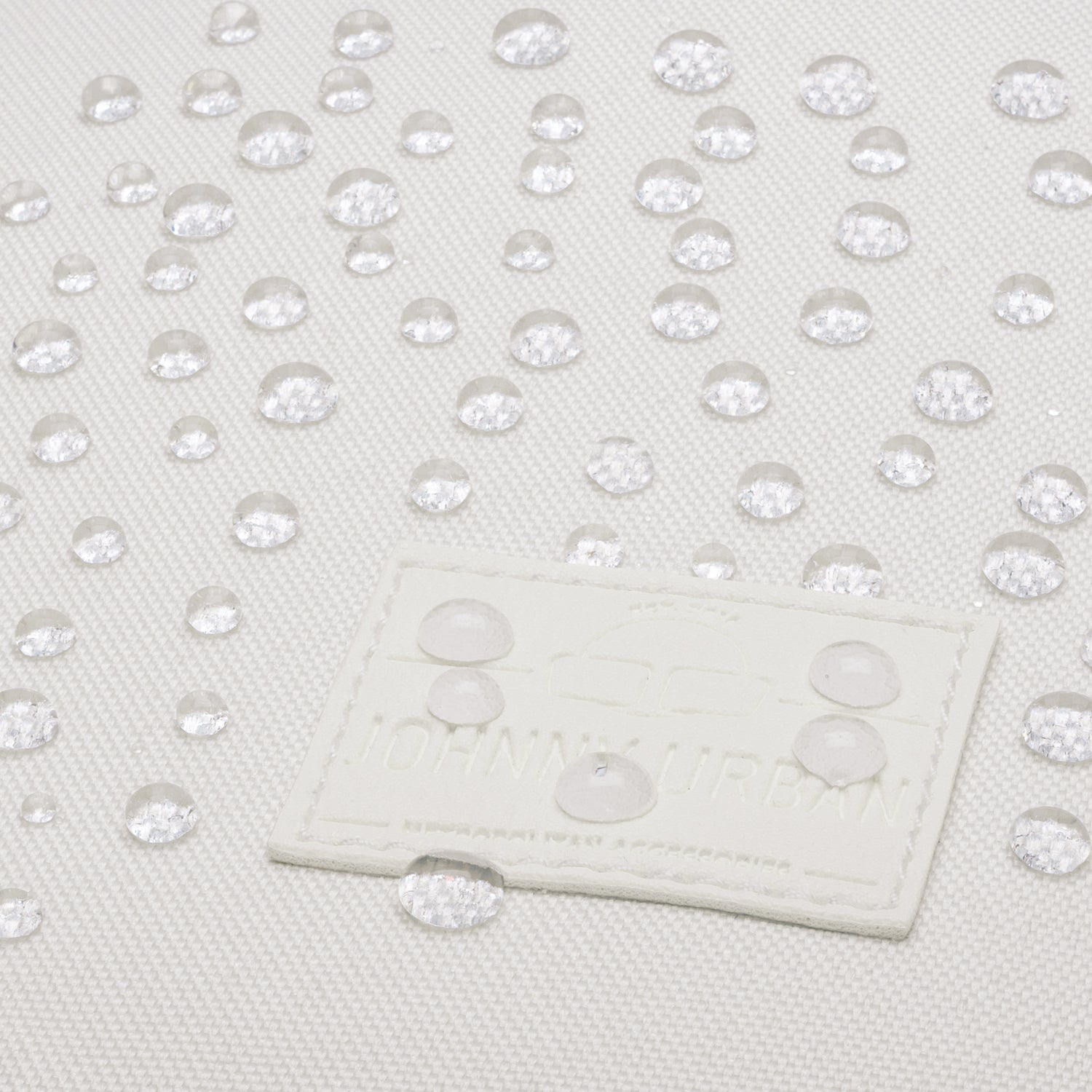 Weiße wasserabweisende Oberfläche mit Wassertropfen und Johnny Urban Logo-Aufnäher