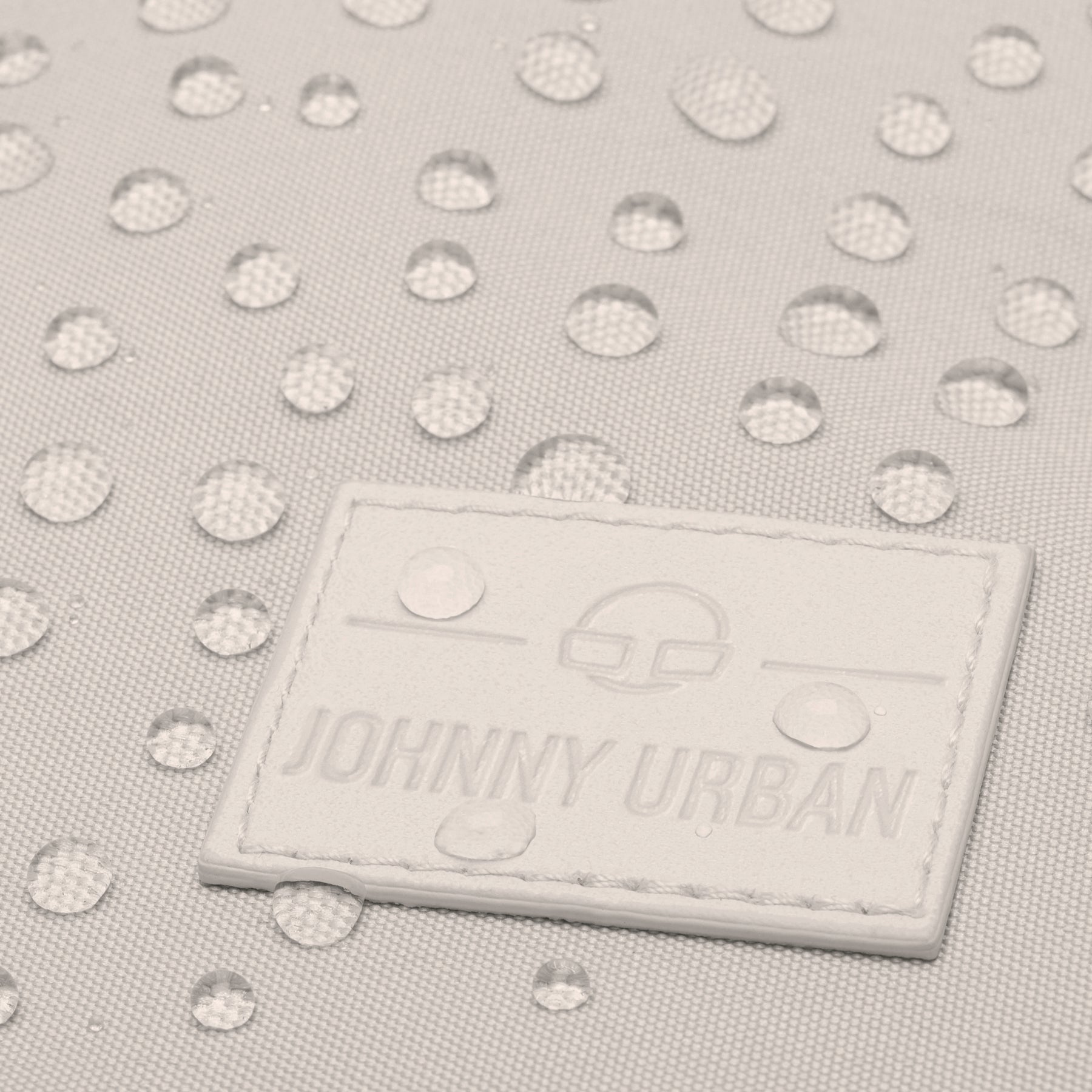 Nahaufnahme des beigen Rucksacks 'Jona Large' mit Wasserperlen auf wasserabweisendem Stoff und Johnny Urban Logo