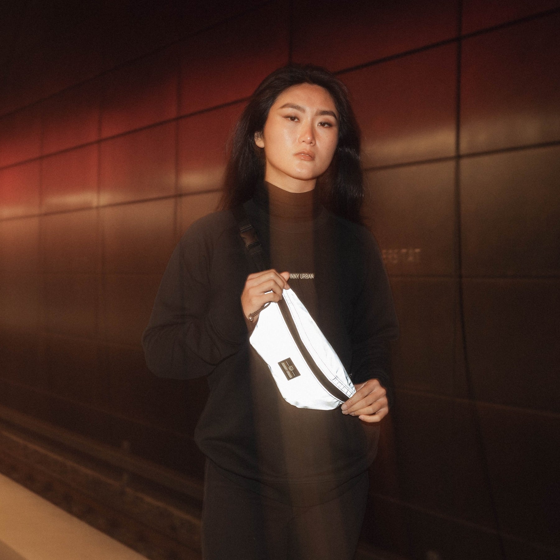 Frau trägt reflektierende Bauchtasche 'Erik Small' vor dunkler Wand