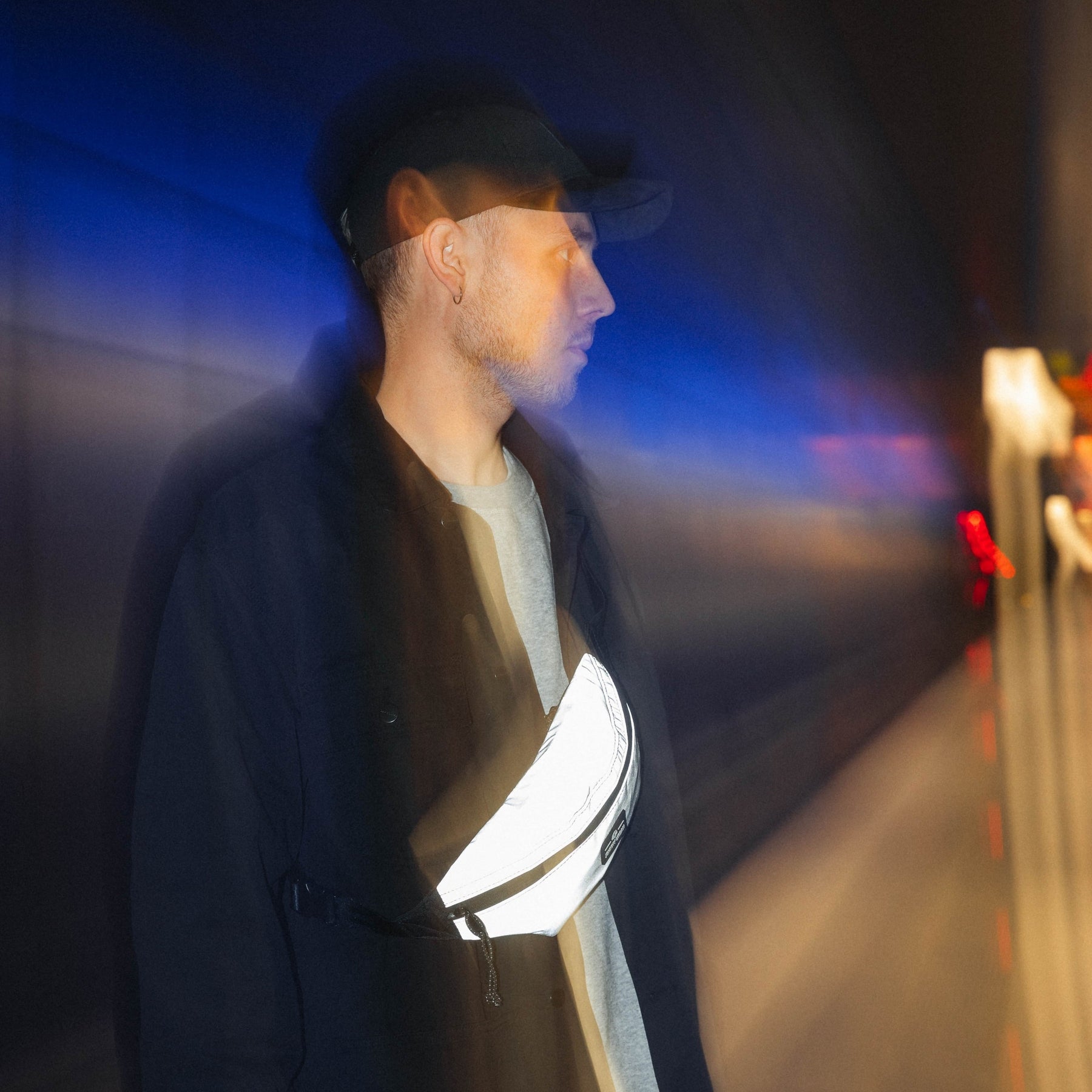 Mann mit reflektierender Bauchtasche 'Erik Small' von Johnny Urban, trägt schwarze Jacke und graues Shirt