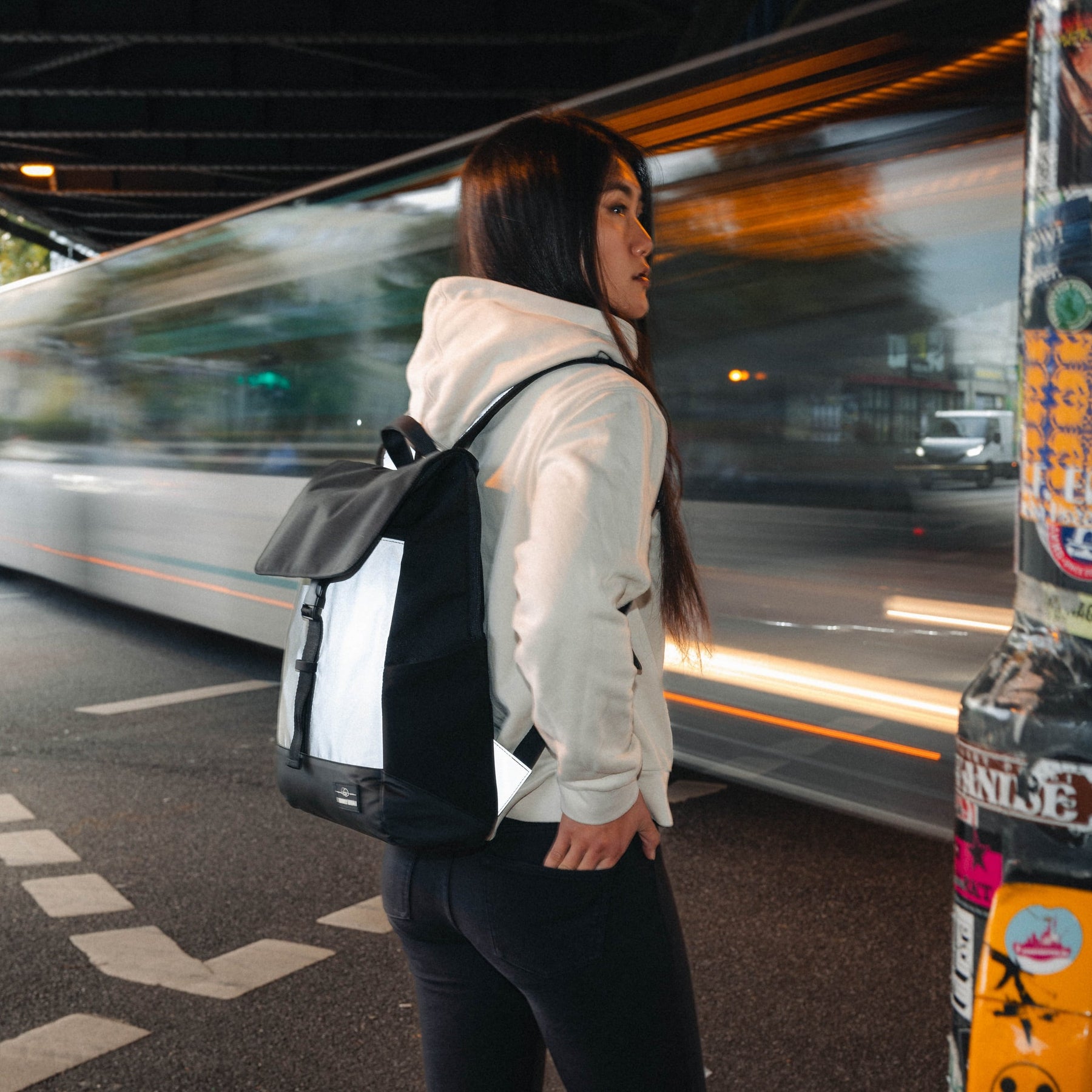 Frau mit reflektierendem Rucksack 'Mika' in Schwarz-Weiß neben einer vorbeifahrenden Straßenbahn