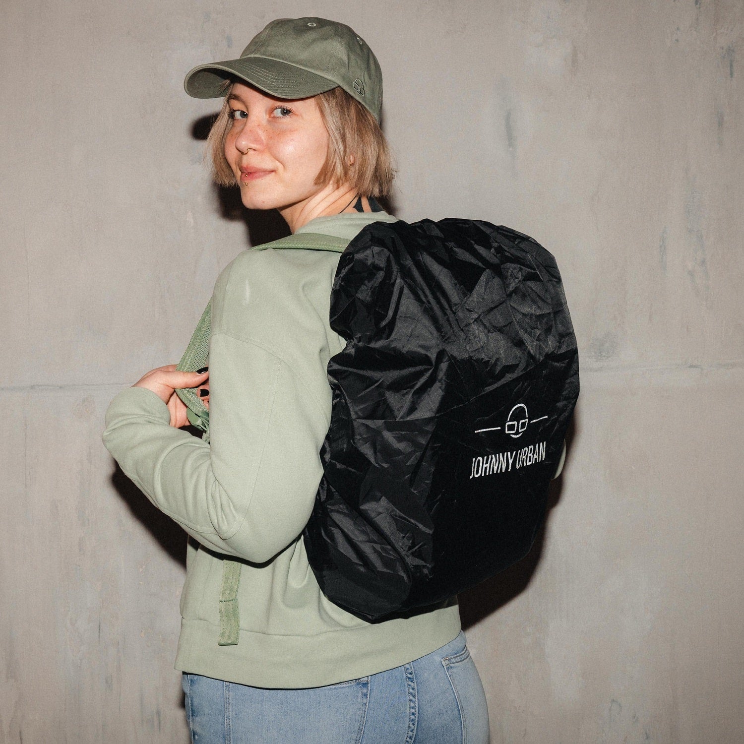 Frau trägt schwarze Johnny Urban Regenschutzhülle 'Bo L' über grünem Pullover und Cap