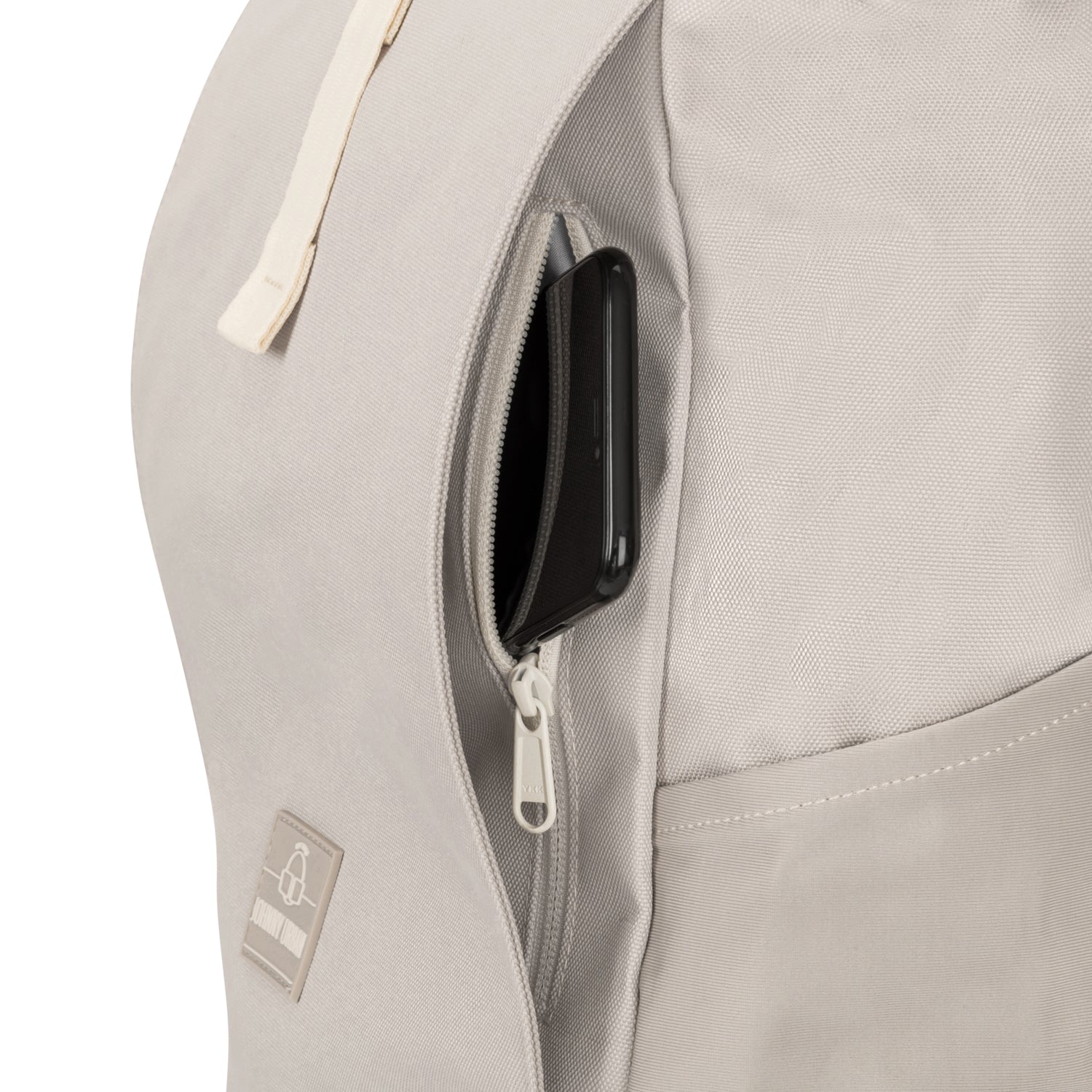 Beiger Rolltop Rucksack Allen Medium mit seitlicher Reißverschlusstasche und einem darin gesteckten Smartphone