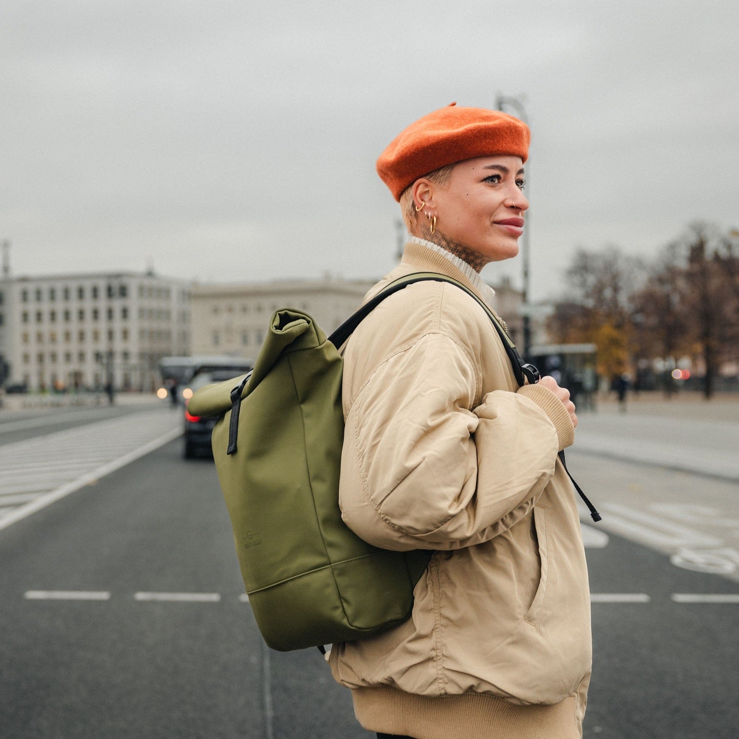 Frau trägt grünen Rolltop-Rucksack 'Harvey Medium' und beige Jacke in urbaner Straße