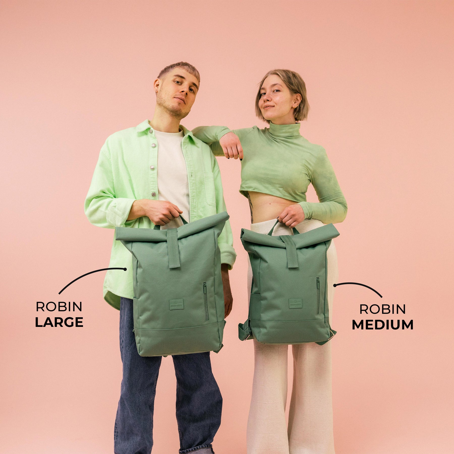 Mann und Frau halten Johnny Urban Rolltop Rucksäcke 'Robin' in großen und mittleren Größen, grün