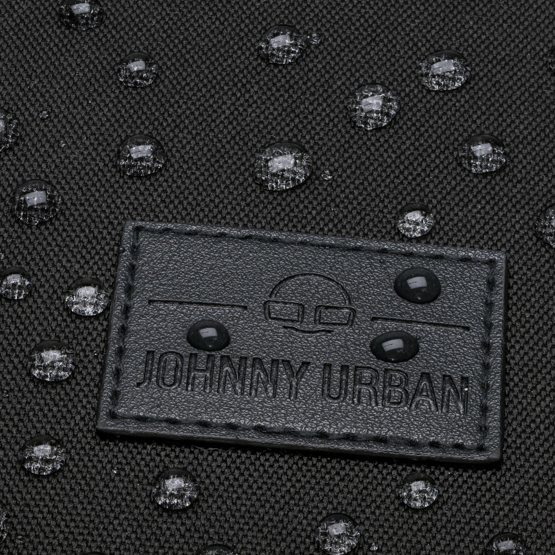Schwarzes wasserabweisendes Material mit aufgenähtem Johnny Urban Logo-Patch und Wassertropfen