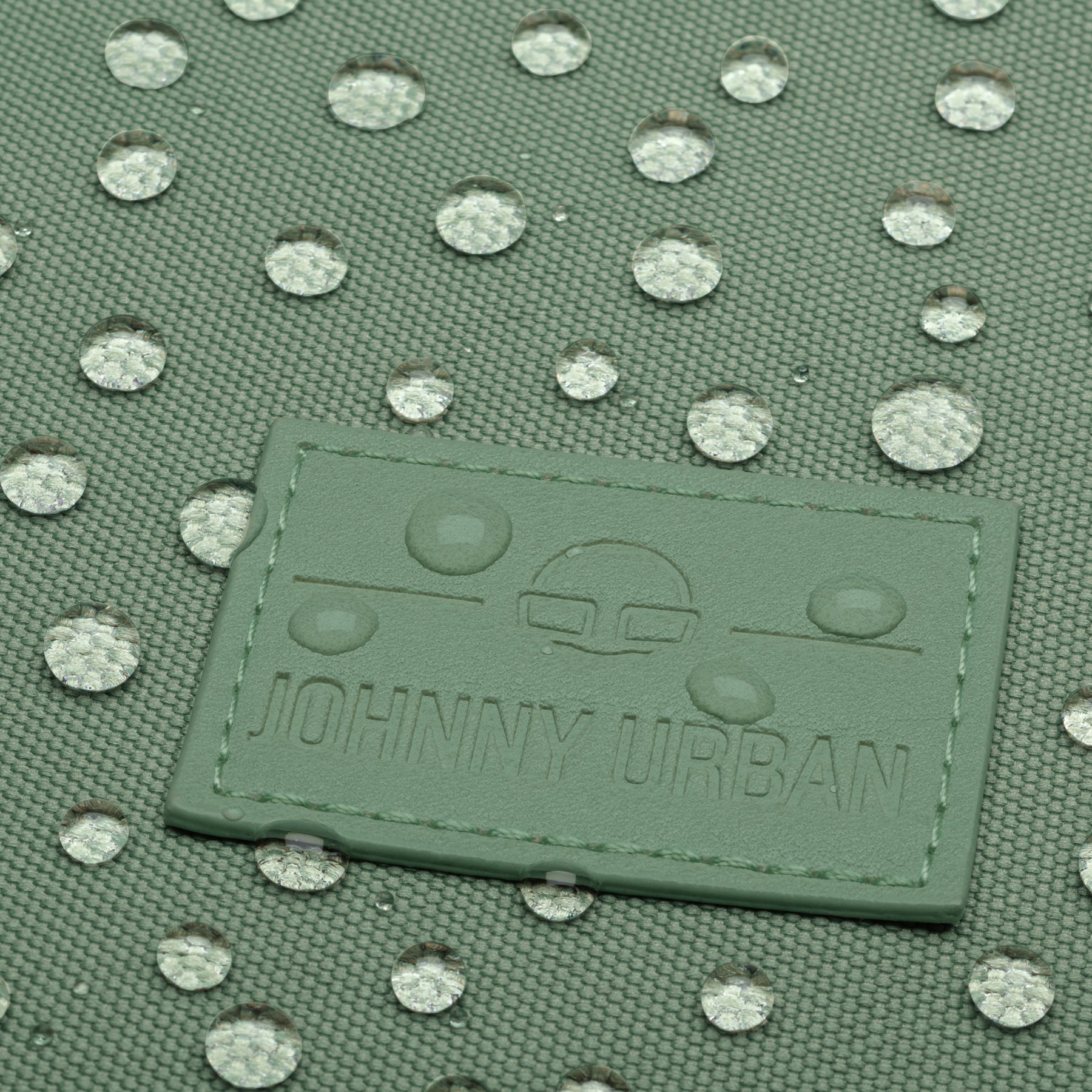 Grünes wasserdichtes Gewebe mit wasserabweisenden Tropfen und Johnny Urban Logo auf einem Rolltop Rucksack