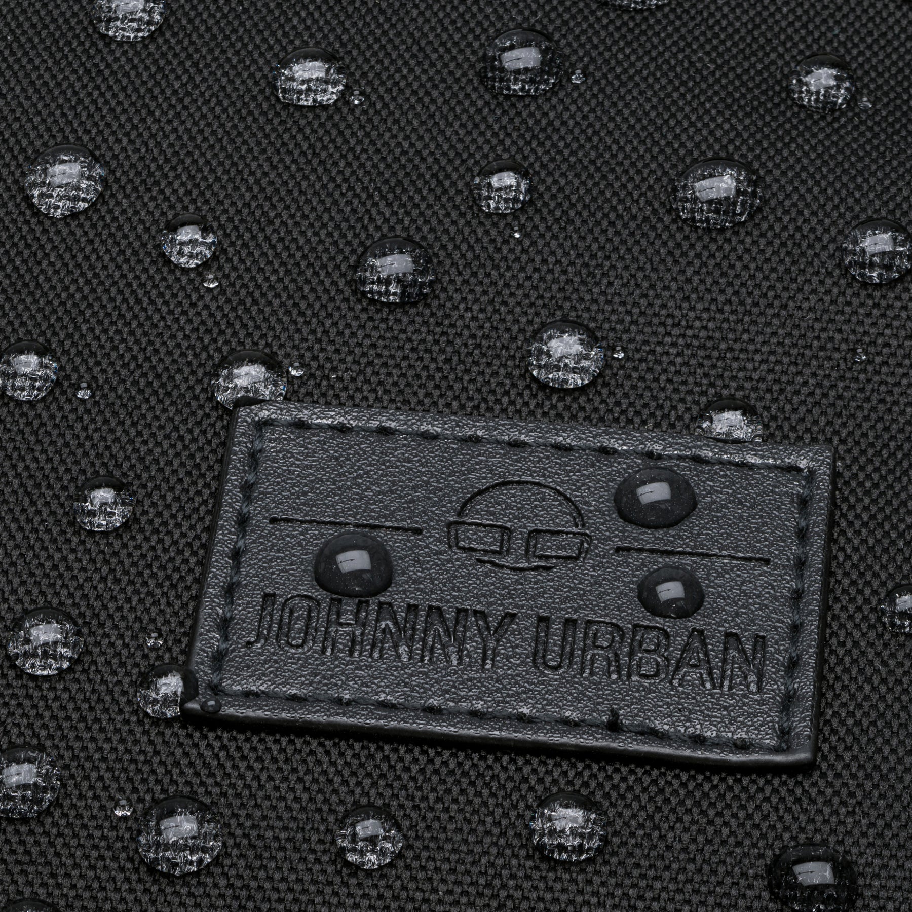 Nahaufnahme eines Gewebematerials mit Johnny Urban Logo und wasserabweisenden Wassertropfen darauf