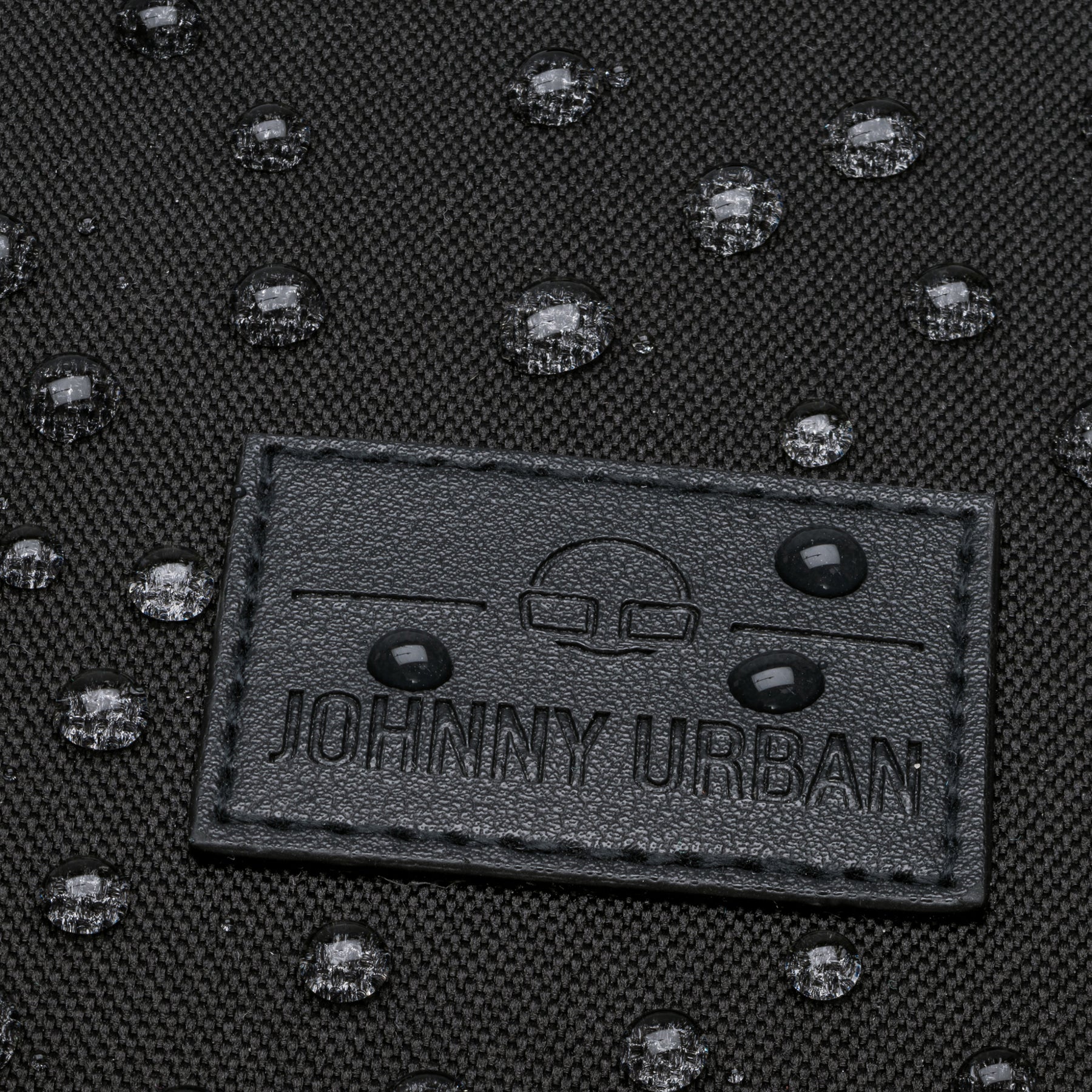 Nahaufnahme des schwarzen Johnny Urban Logos auf einem wasserabweisenden Rolltop-Rucksack 'Robin Medium' mit Wassertropfen