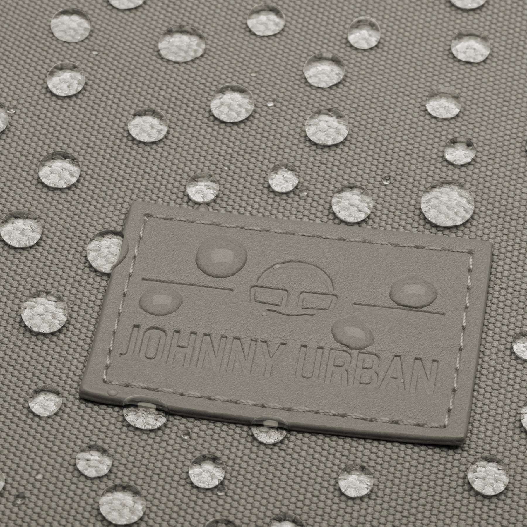 Nahe Aufnahme eines wasserdichten Johnny Urban Rolltop Rucksacks mit sichtbaren Wassertropfen auf dem grauen Gewebe