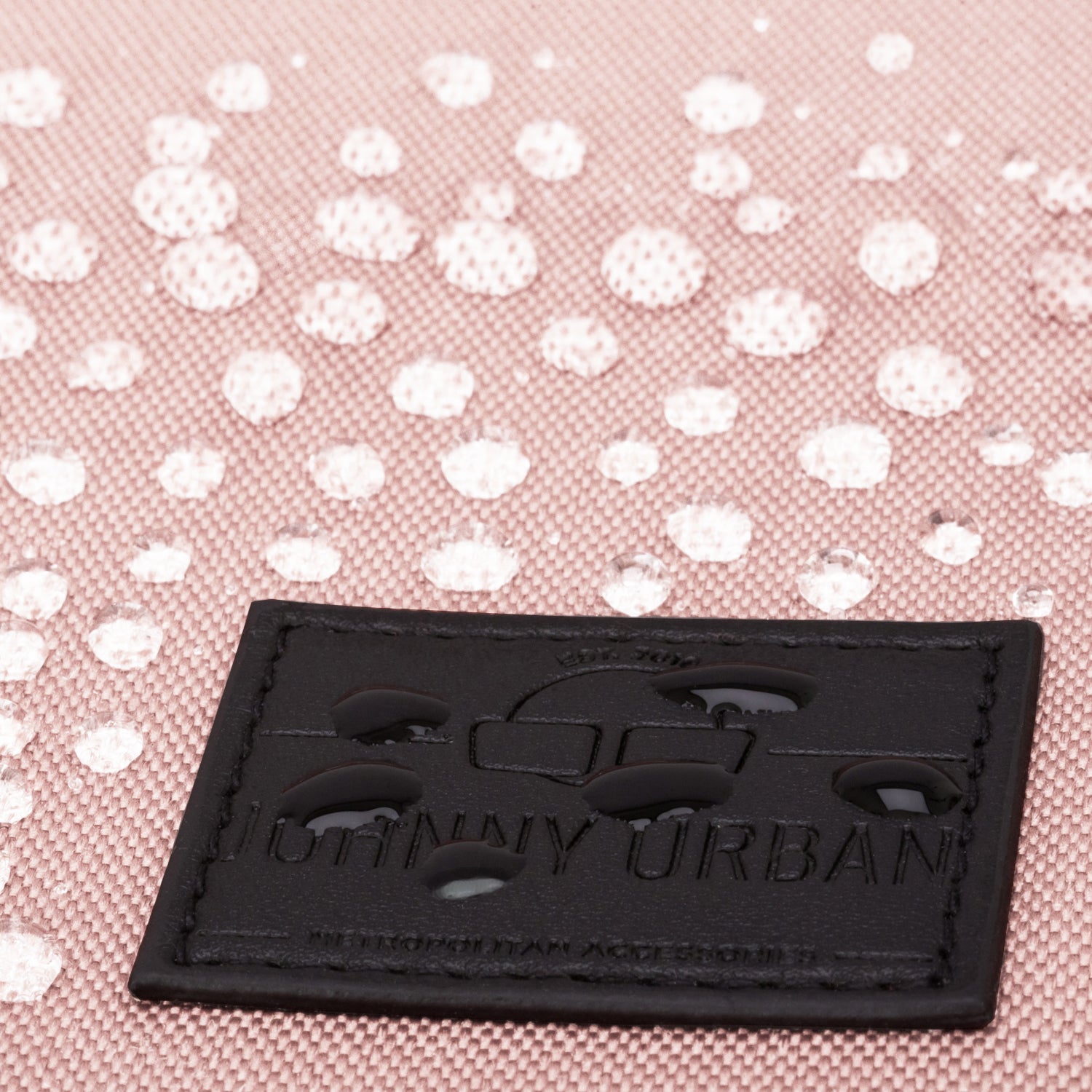 Nahaufnahme des schwarzen Lederlabels mit Prägung auf einem rosa Rucksack mit Wassertröpfchen