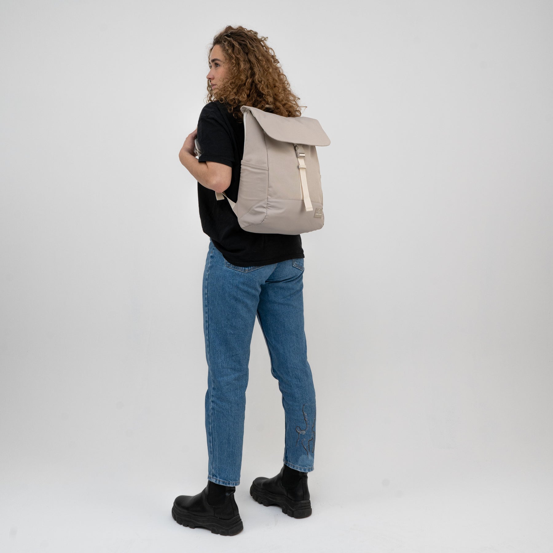 Frau mit beigem Rucksack 'Mika', blauer Jeans mit Stickerei und schwarzem T-Shirt von hinten