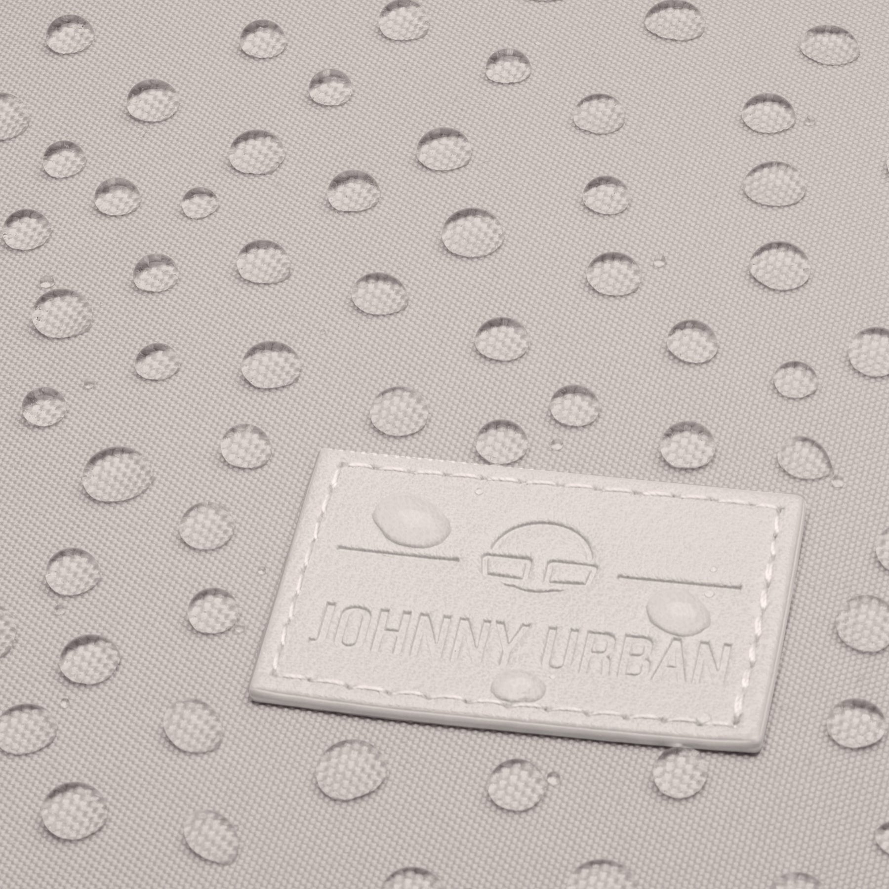 Nahaufnahme von wasserabweisendem beigem Stoff mit Wassertröpfchen und Johnny Urban Markenetikett