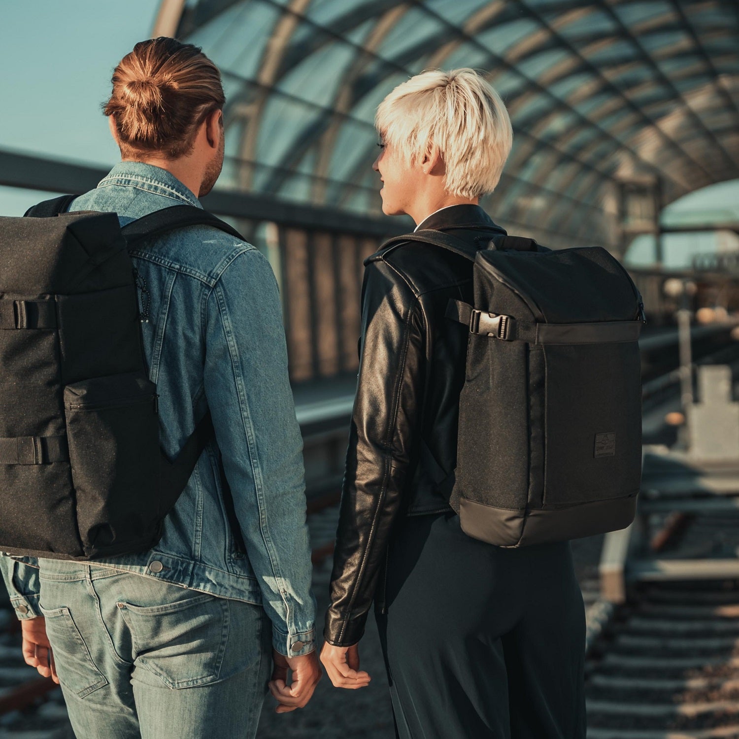 Zwei Personen auf einem Bahnhofsgleis, tragen beide schwarzen Rucksack 'Luca' von Johnny Urban, eine Person in Jeansjacke, andere in Lederjacke
