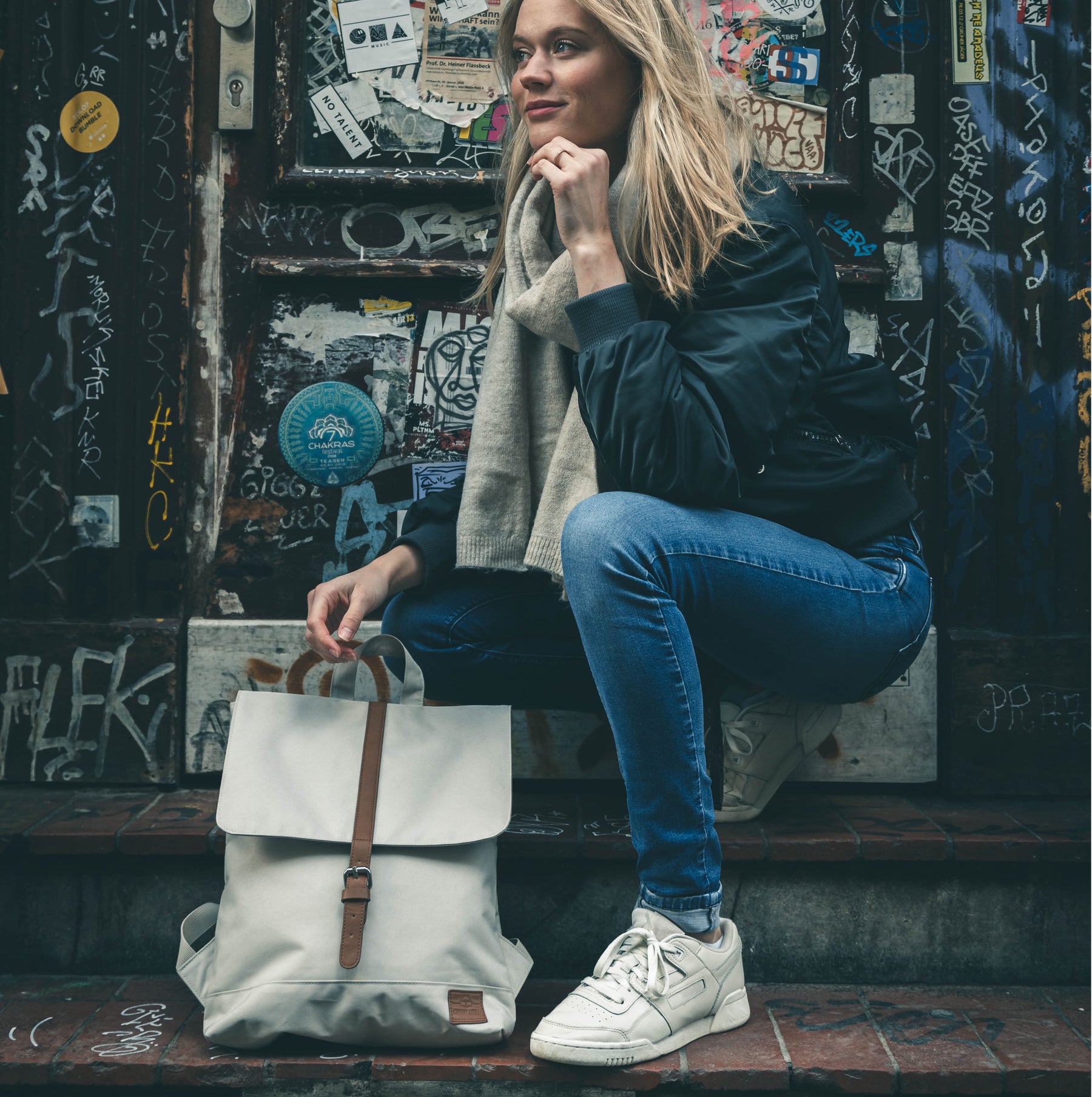 Frau hockt in urbaner Umgebung und hält beigen Damenrucksack 'Mia' mit braunem Lederriemen