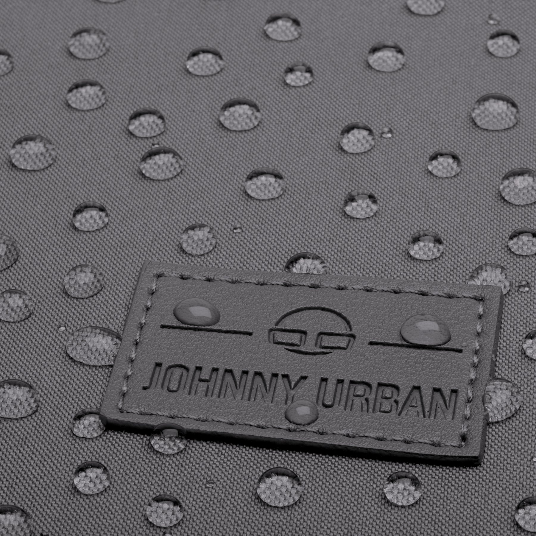Detailaufnahme des wasserabweisenden grauen Gewebes und des Johnny Urban Logos auf dem Rucksack Jona Large