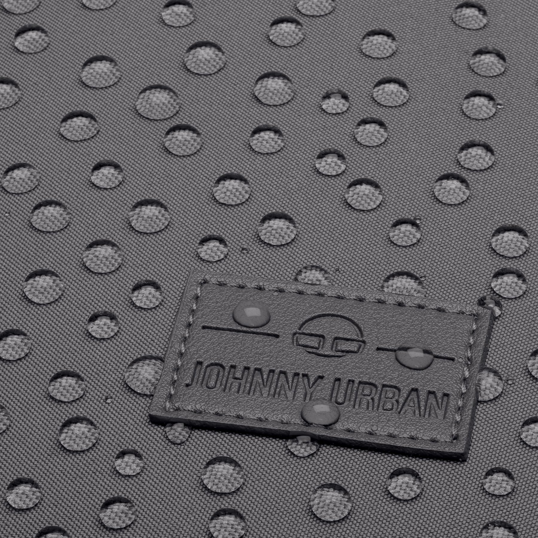 Nahaufnahme eines grauen wasserabweisenden Rucksacks Jona Medium mit Johnny Urban Logo und Wasserperlen