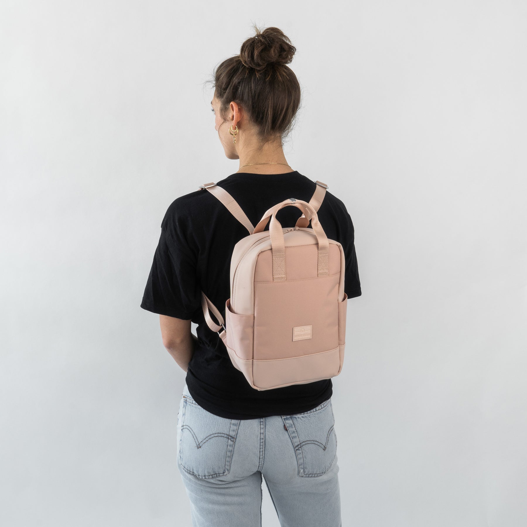 Frau trägt kleinen hellrosa Rucksack 'Jona Small' mit Taschen, schwarzes T-Shirt, helle Jeans