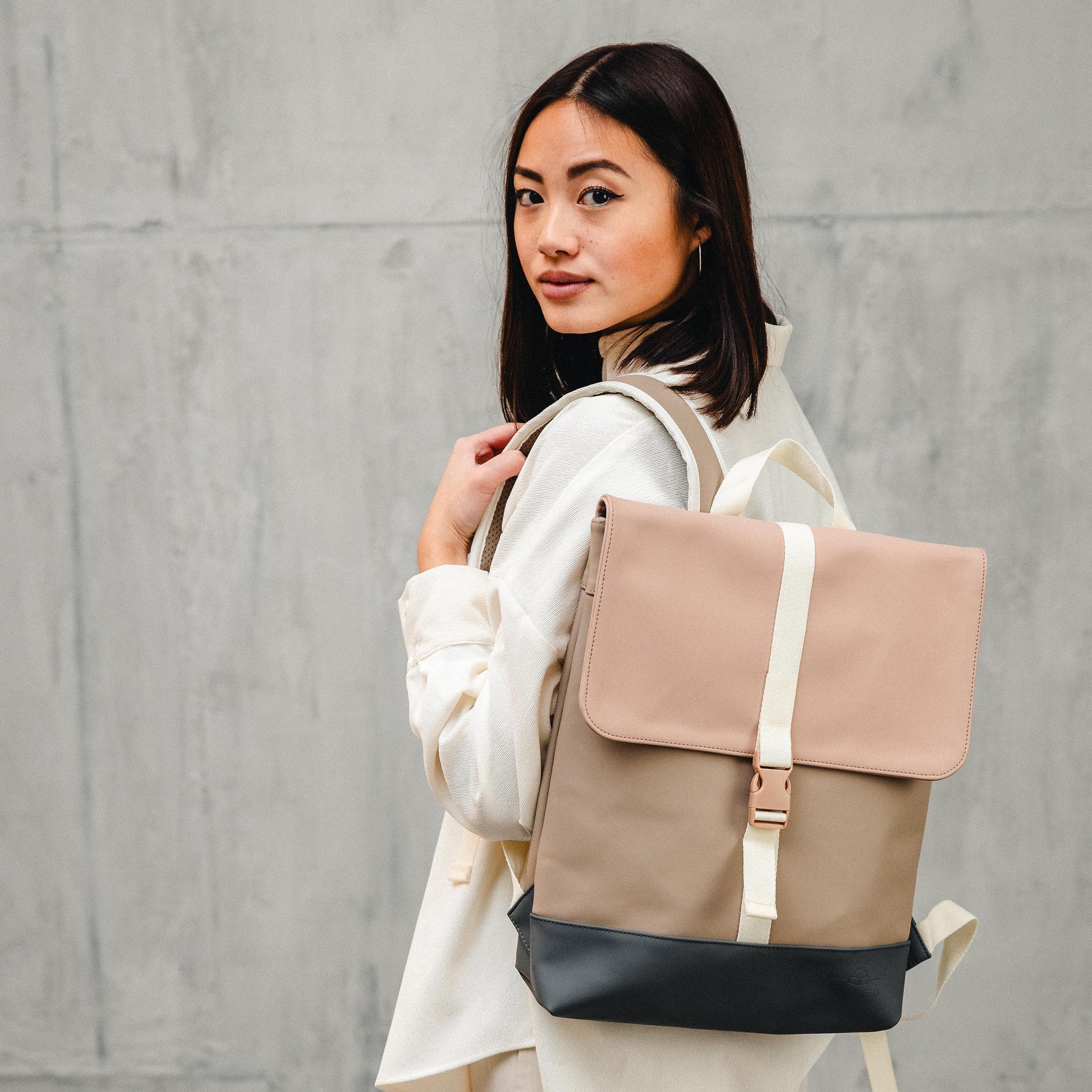 Frau mit beige-schwarzem Rucksack Damen 'Ruby' vor grauer Wand