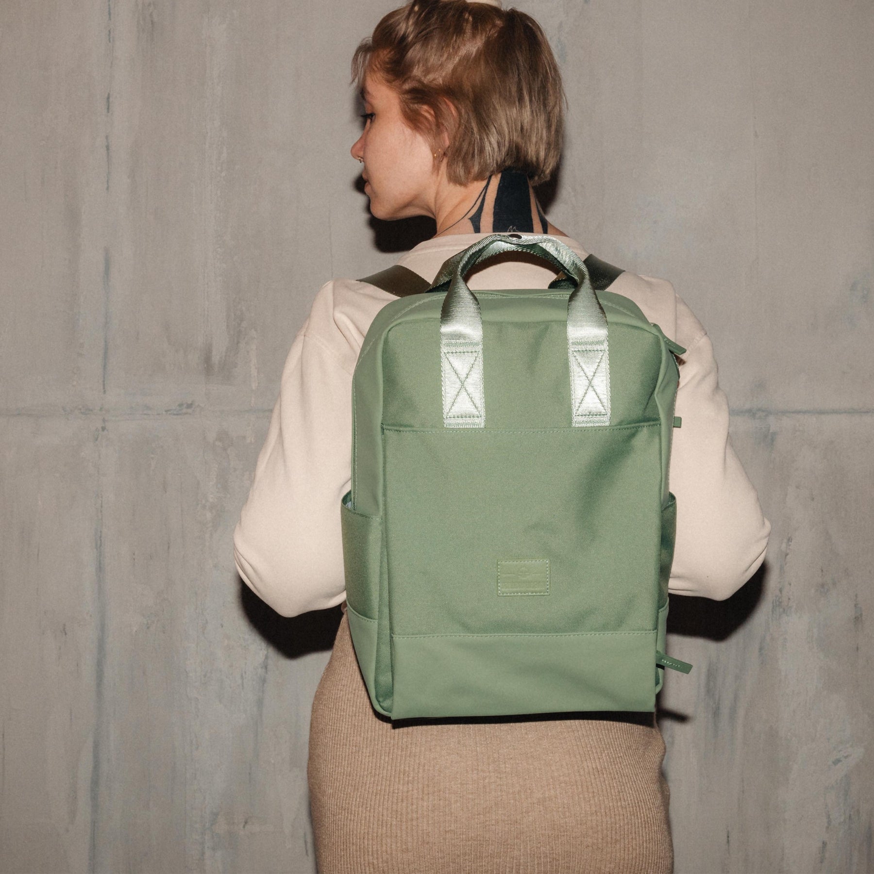 Frau trägt grünen nachhaltigen Rucksack 'Jona Large' von Johnny Urban vor grauer Wand