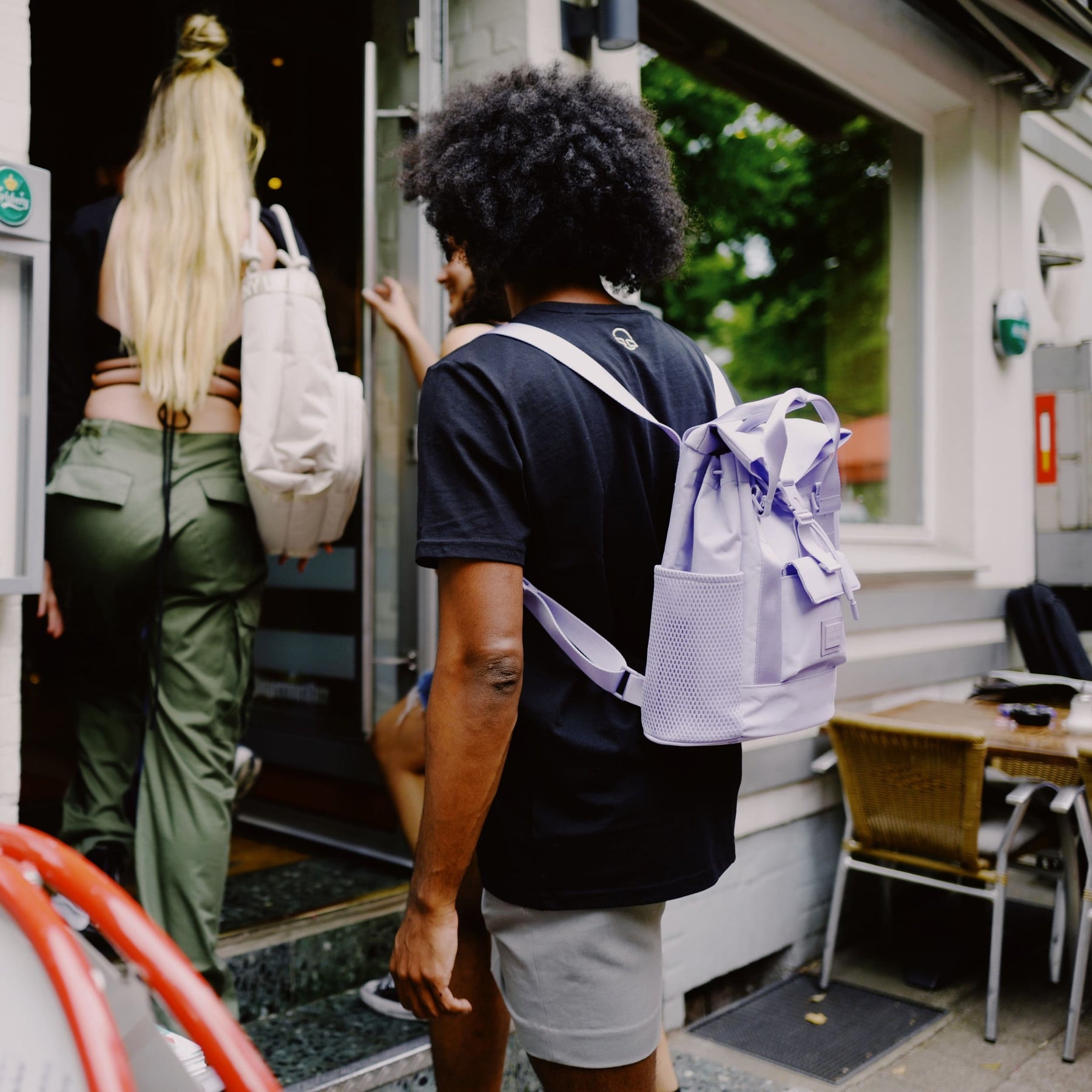 Person mit schwarzem T-Shirt trägt lila Rucksack 'Jules' von Johnny Urban, andere Personen gehen voran in ein Gebäude