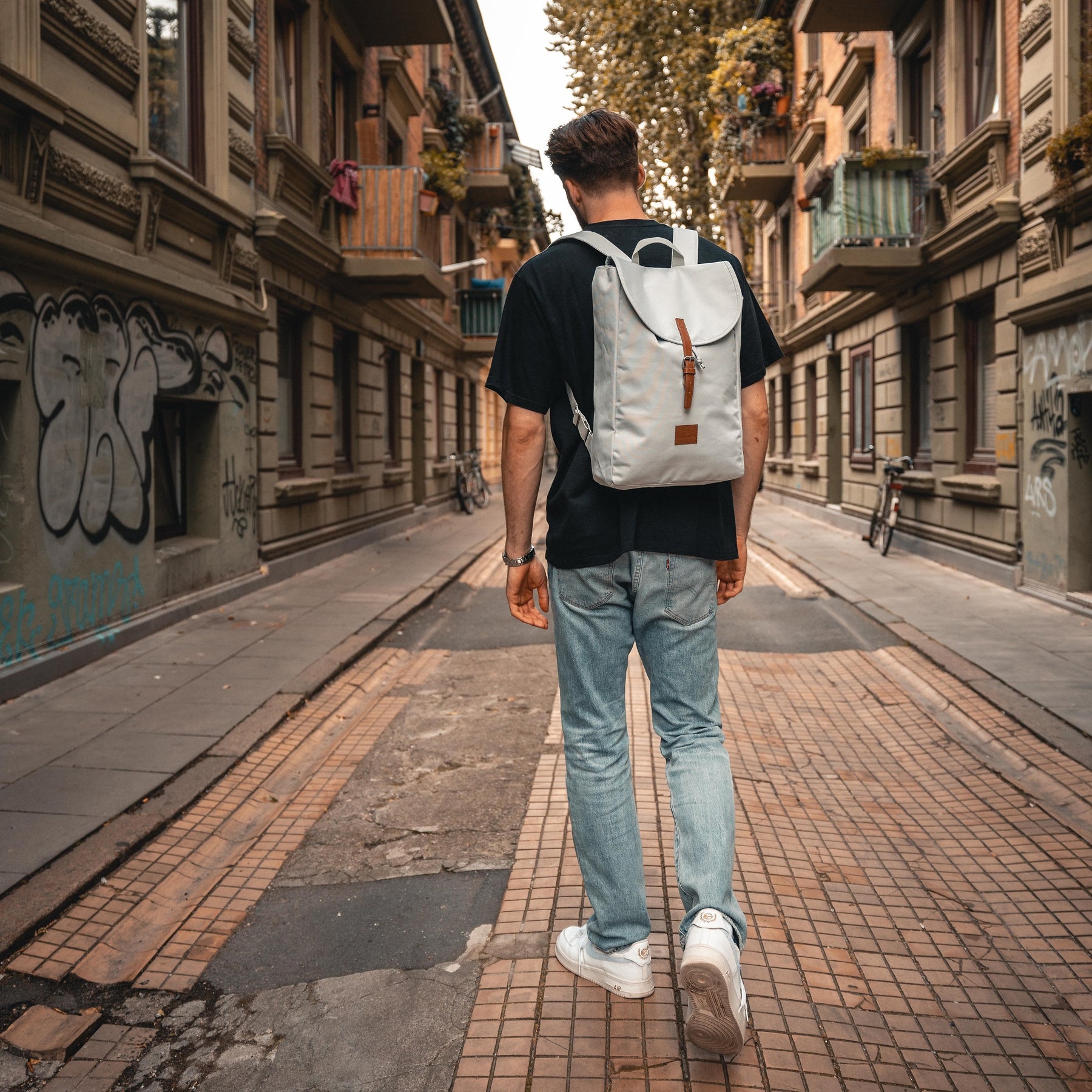Mann trägt grauen Rucksack 'Liam' mit Lederdetail in urbaner Straße