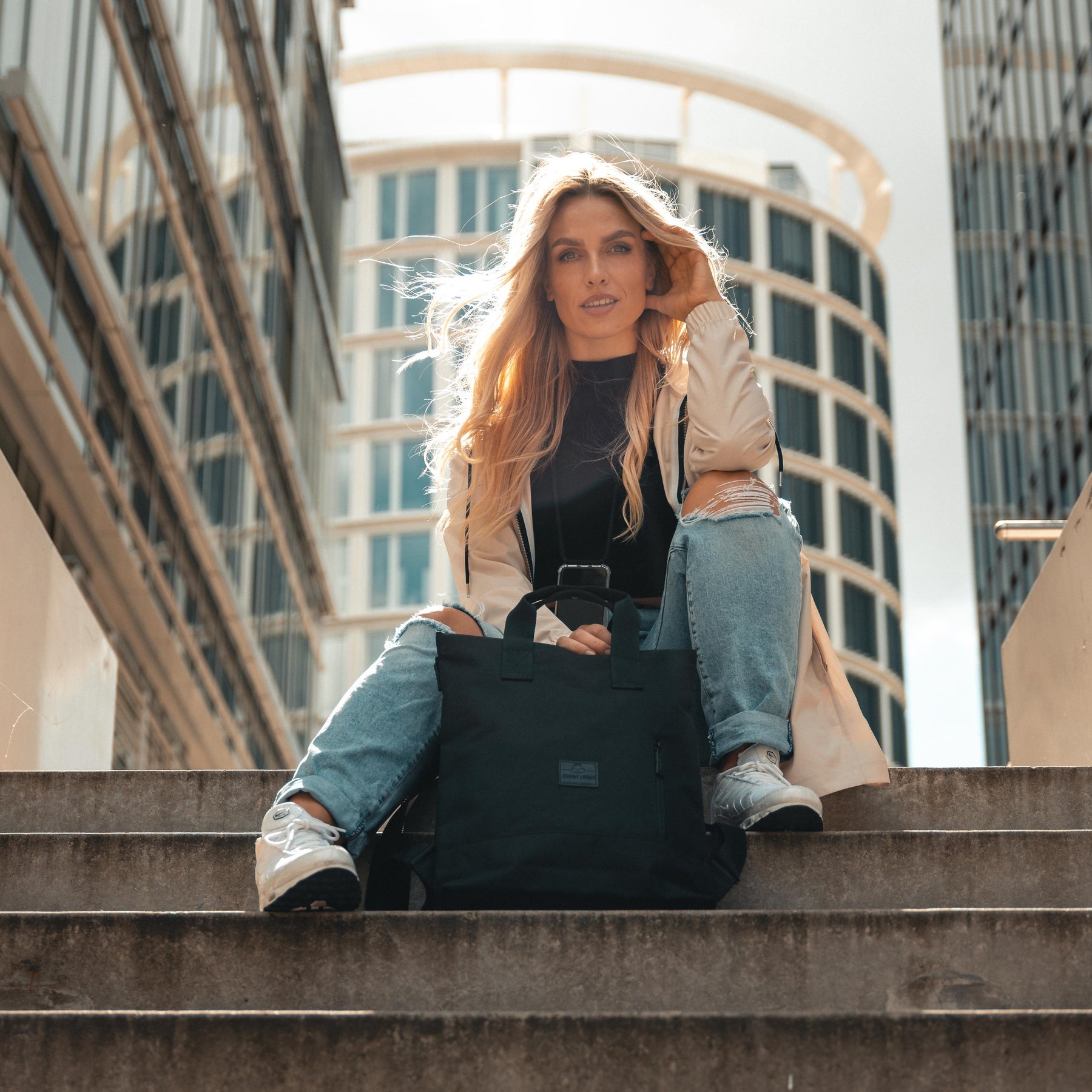 Frau sitzt auf Treppe in Stadt mit schwarzem Johnny Urban Rucksack 'Ivy' auf dem Boden
