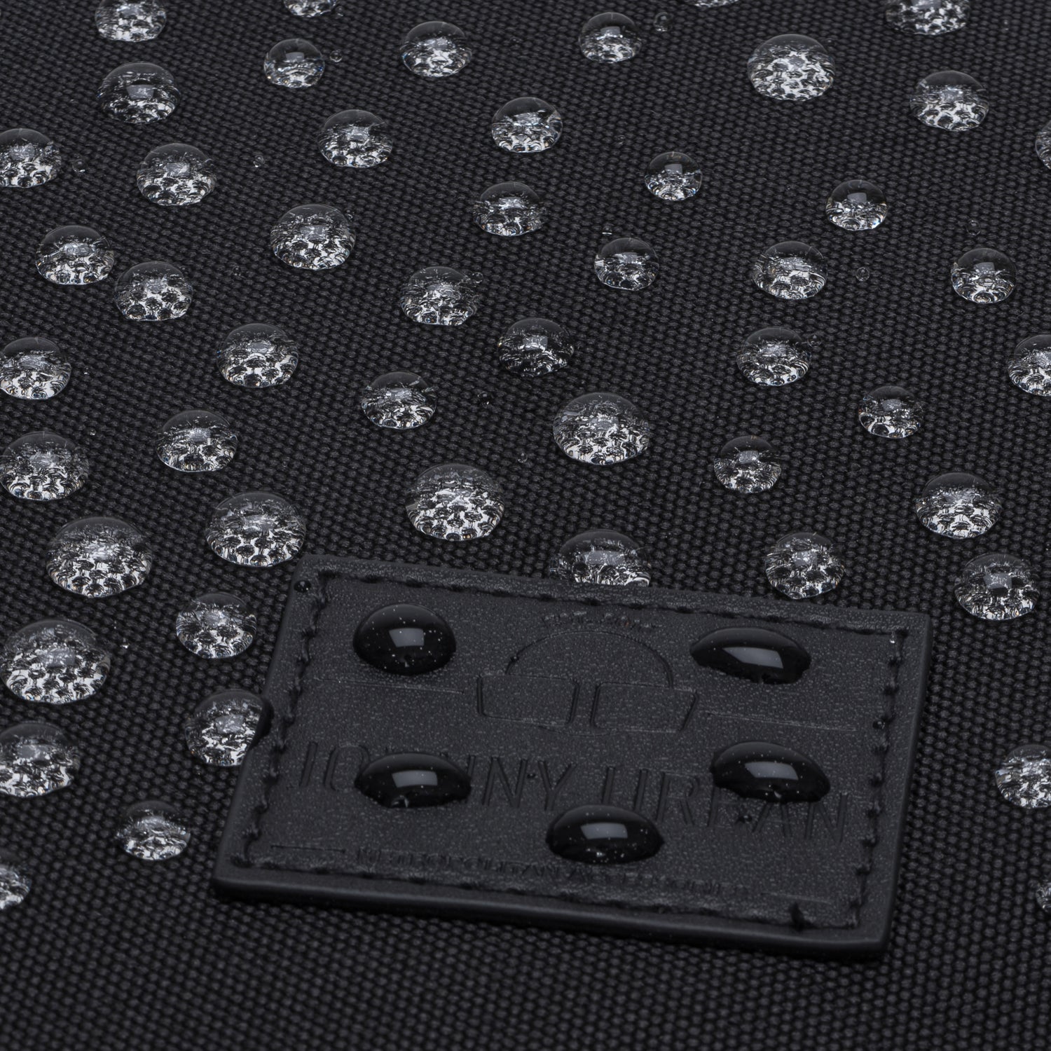 Wasserabweisende schwarze Textiloberfläche mit Wassertropfen und Johnny Urban Logoetikett