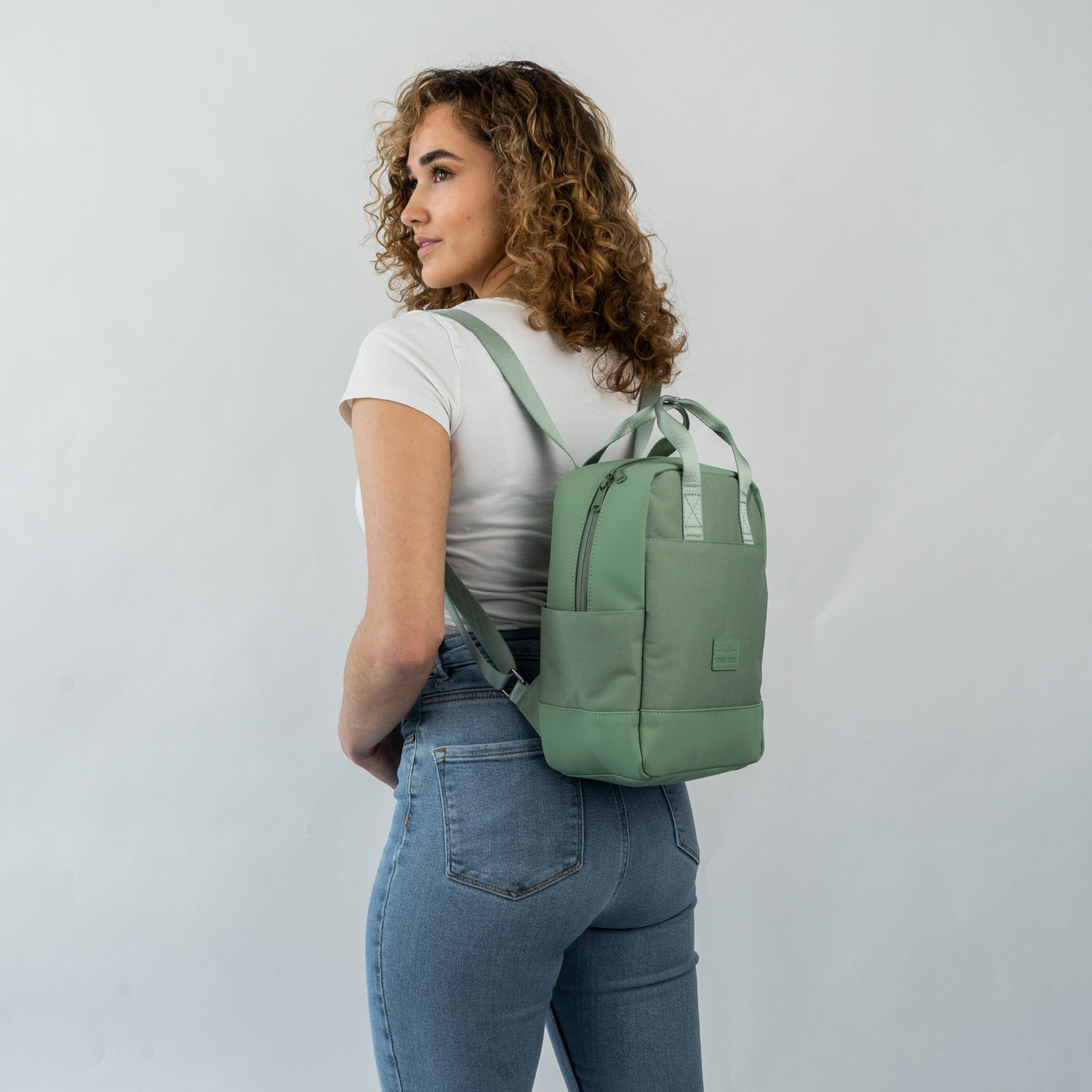 Frau mit lockigem Haar, die den kleinen, nachhaltigen Jona Small Rucksack in grün trägt
