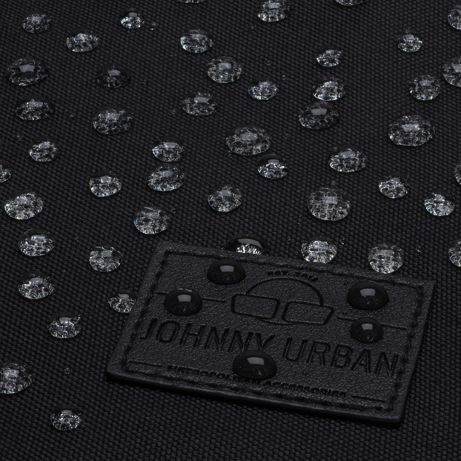 Nahaufnahme von wasserabweisendem schwarzem Stoff mit Johnny Urban Logo und Wassertropfen