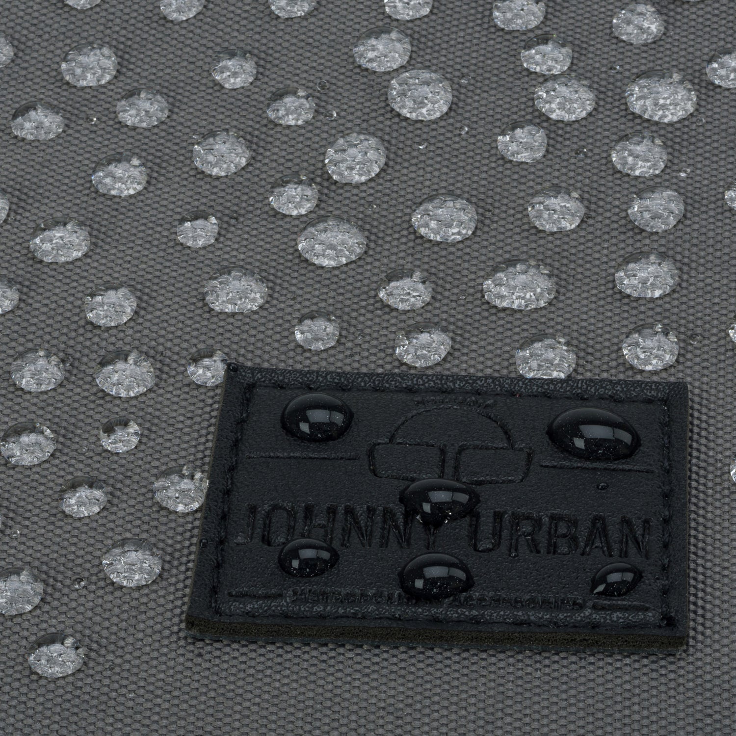 Nahaufnahme des wasserabweisenden Materials des Rucksacks 'Oskar' mit Wassertropfen und schwarzem Johnny Urban Logo