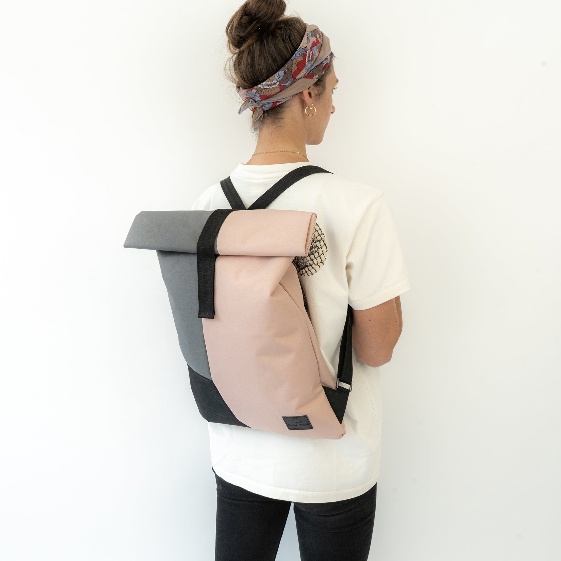 Frau mit pink-grauem Rolltop-Rucksack 'Oskar' von Johnny Urban, trägt weißen T-Shirt und schwarzen Jeans