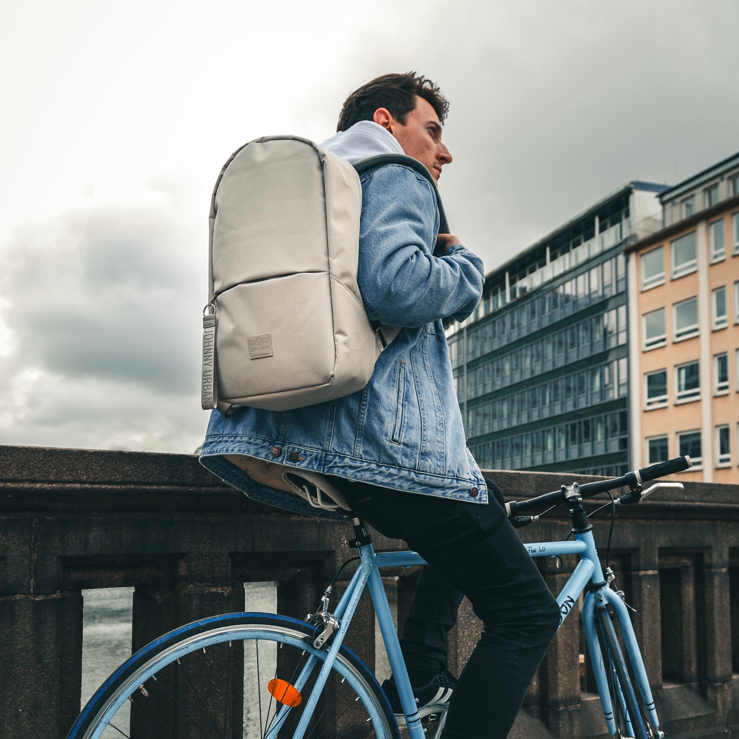 Jugendlicher sitzt auf hellblauem Fahrrad trägt grauen Johnny Urban Rucksack 'Milo' und Jeansjacke