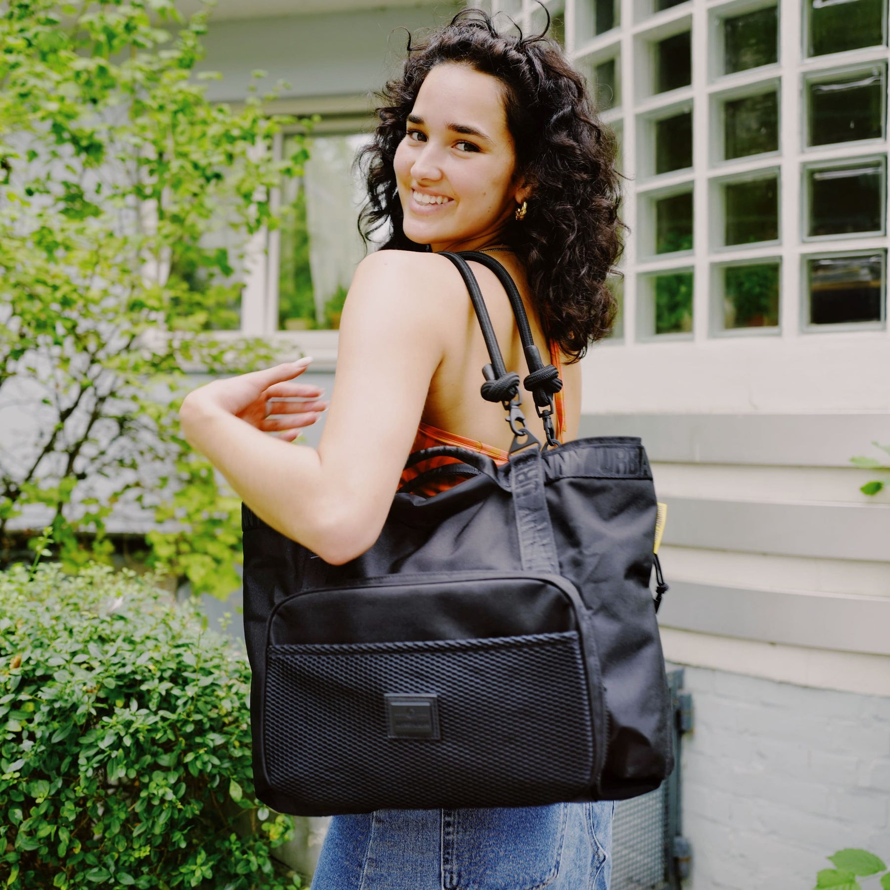 Frau mit schwarzer Shopper Tasche 'Cassie' von Johnny Urban vor Haus mit Pflanzen