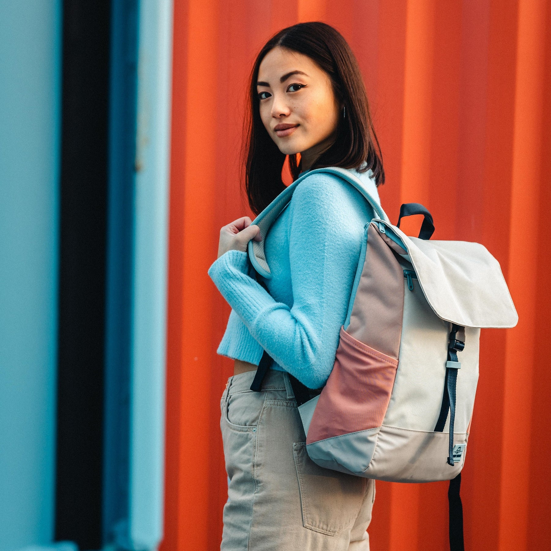 Frau trägt den Tagesrucksack 'Mika' in Sand- und Rosatönen vor orangener Wand