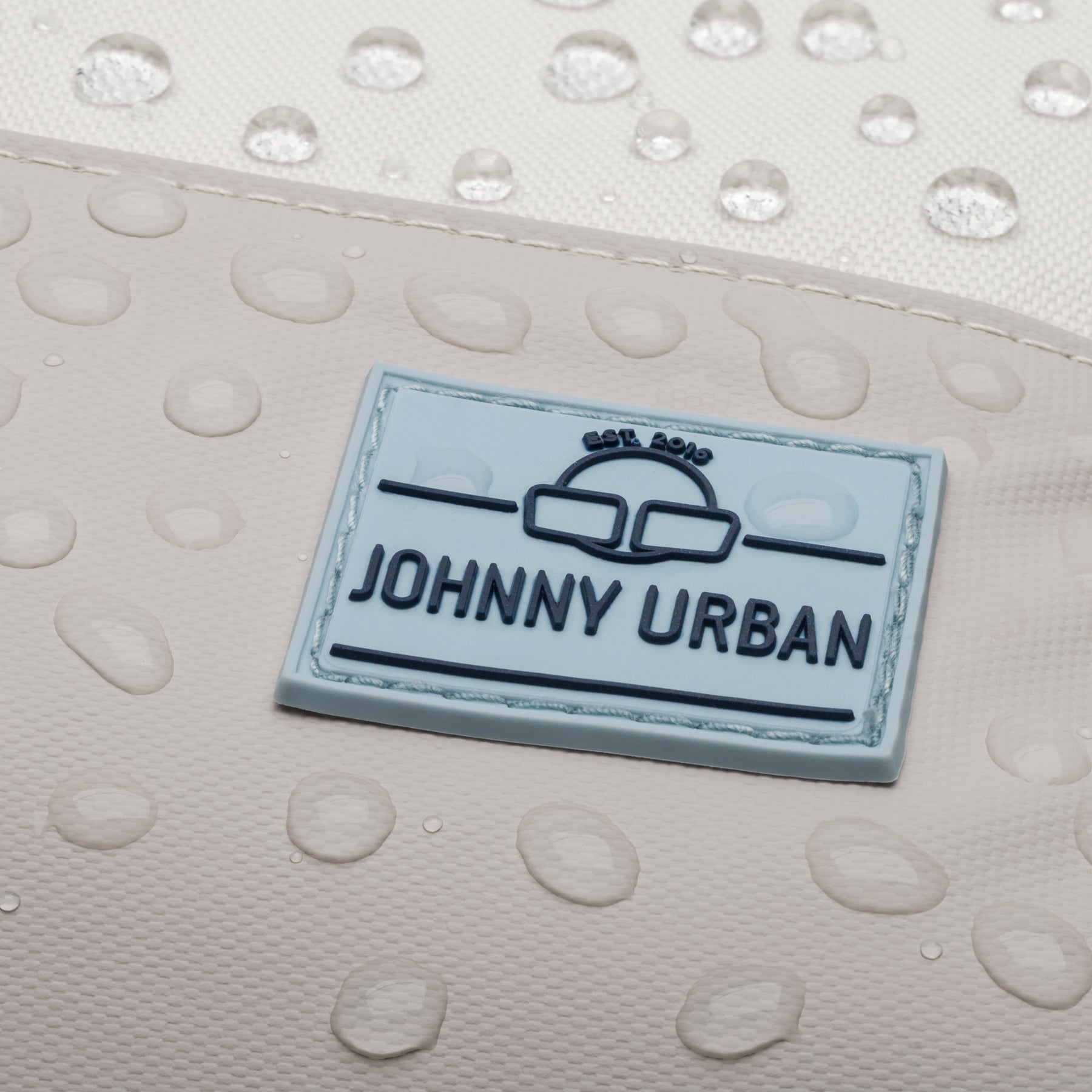 Nahaufnahme des wasserabweisenden Materials und des Johnn Urban Logos auf dem Rucksack 'Mika' in Beige