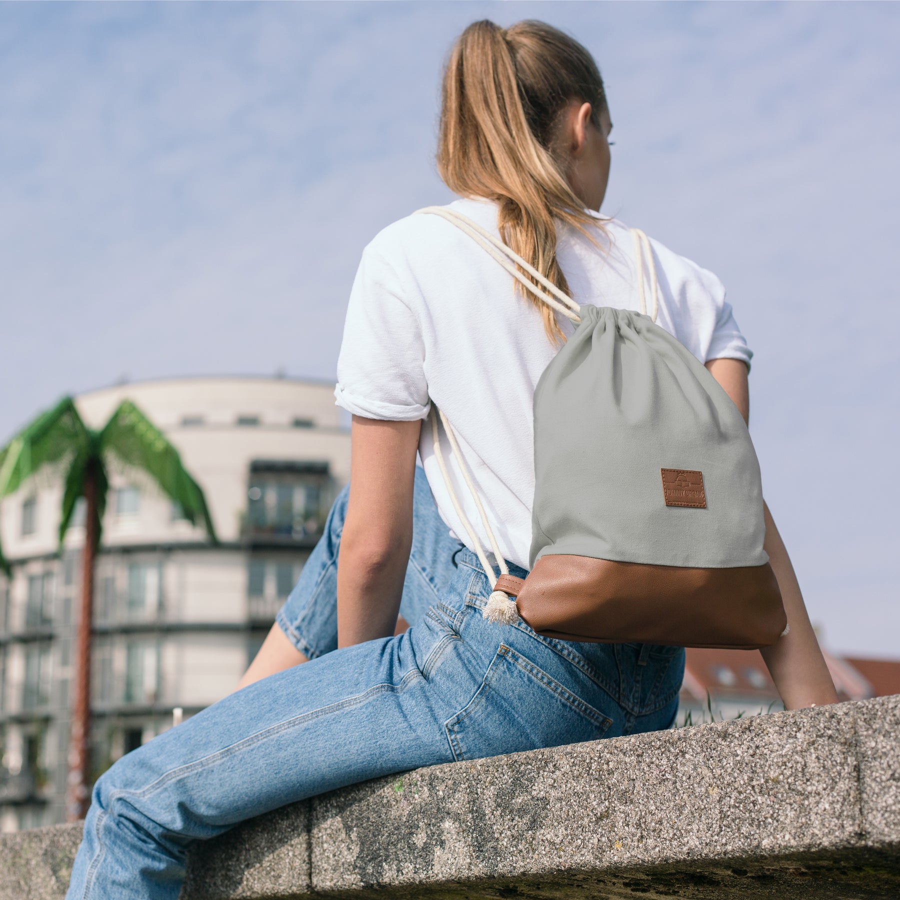Frau mit grauem Turnbeutel 'Luke' mit braunem Boden sitzt auf Betonmauer urban