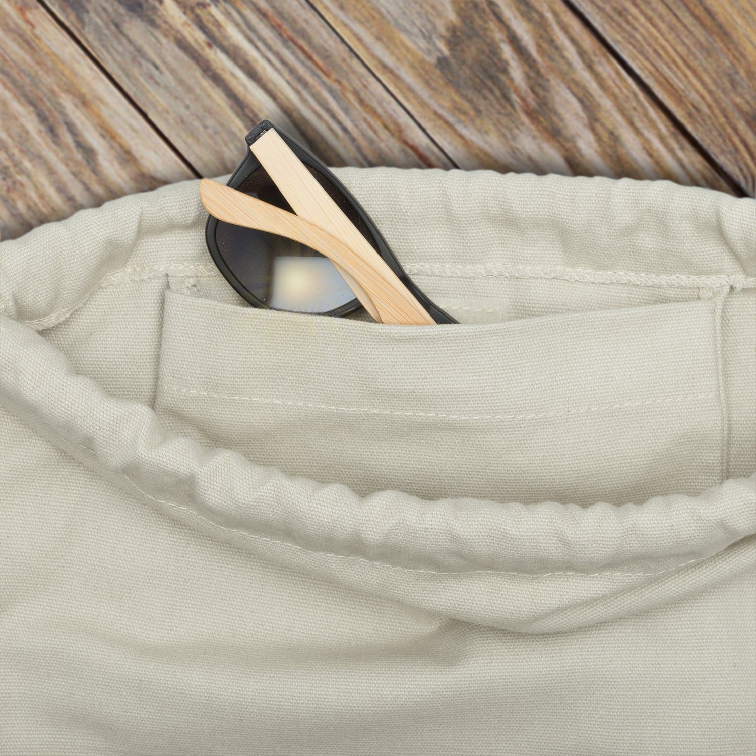 Beige Turnbeutel 'Luke' mit seitlicher Tasche, in der schwarze Sonnenbrille mit hellen Bügeln steckt