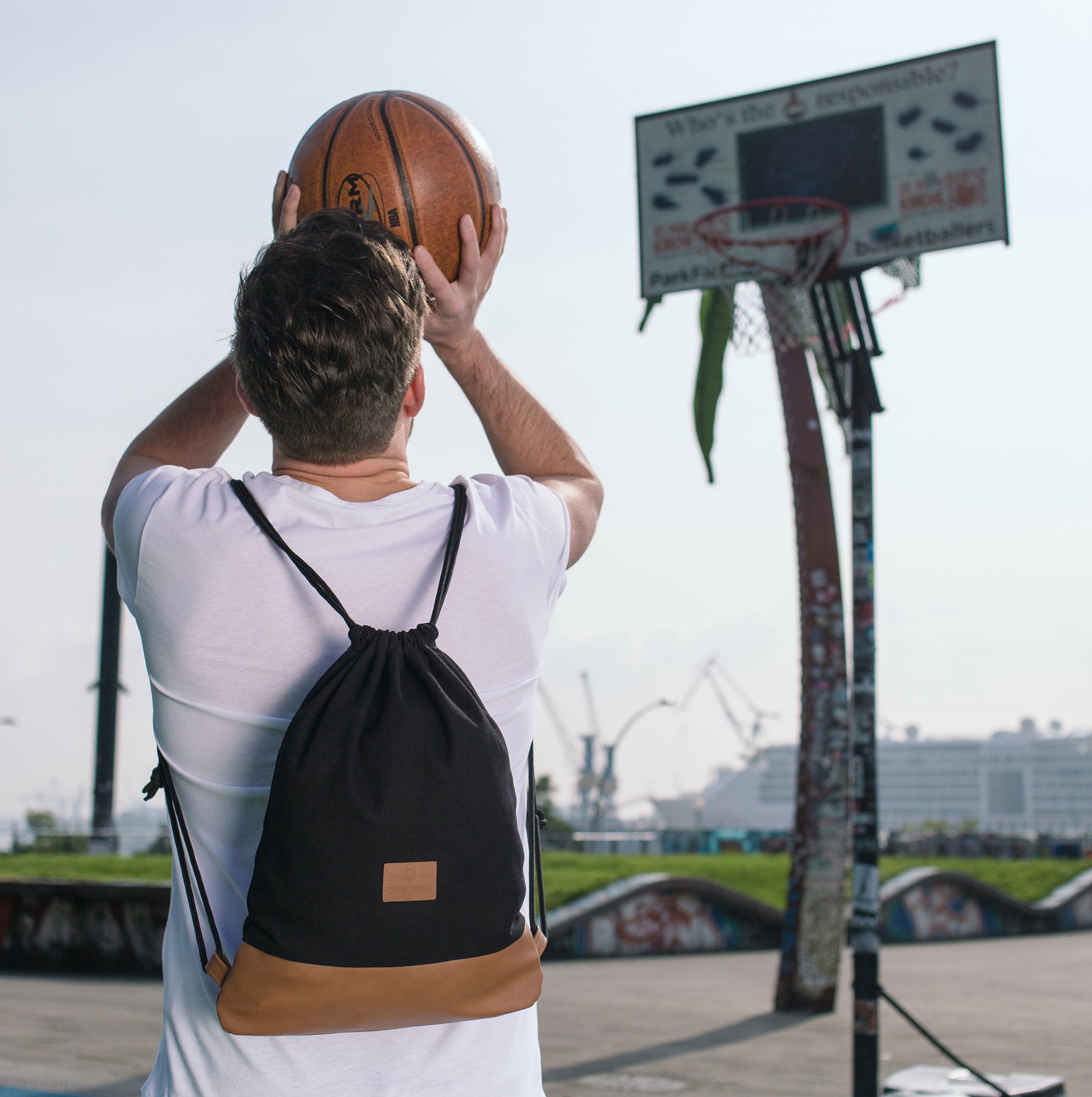 Mann mit weißem T-Shirt spielt Basketball und trägt schwarzen Turnbeutel 'Luke' mit braunem Boden von Johnny Urban