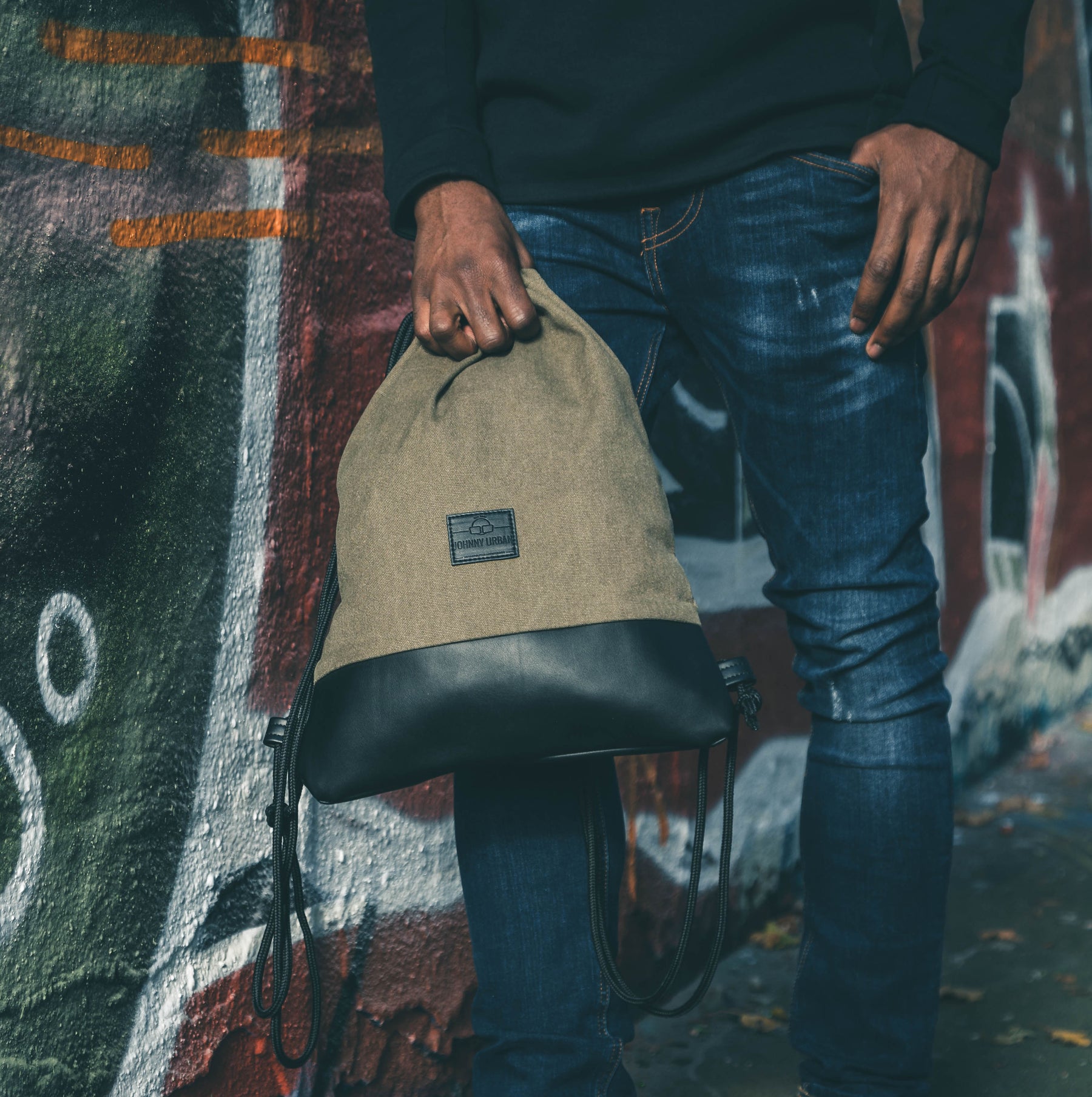 Mann hält den grünen-khaki Turnbeutel 'Luke' von Johnny Urban vor einer Wand mit Graffiti