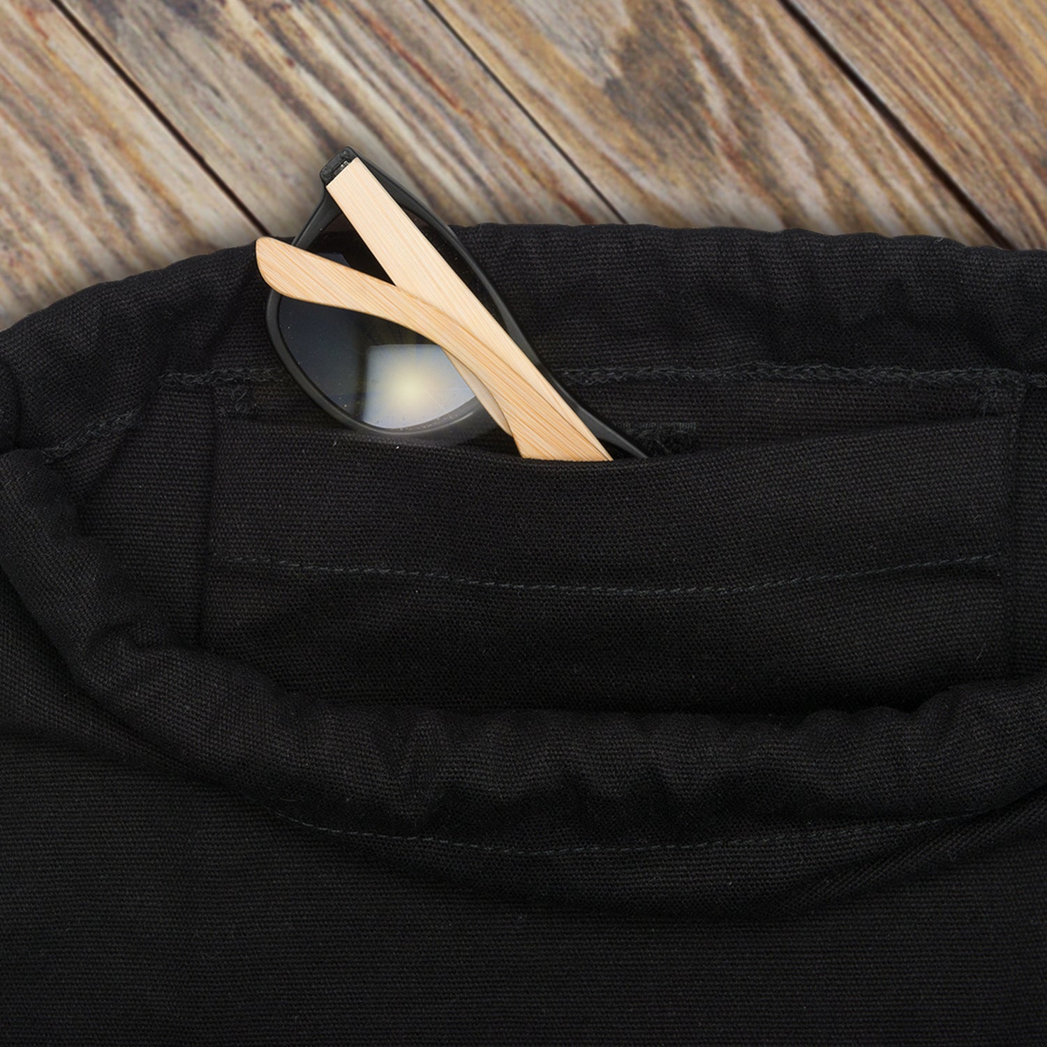 Schwarzer Turnbeutel Luke mit Außentasche, in der eine Brille mit schwarzem Gestell und hellen Bügeln steckt